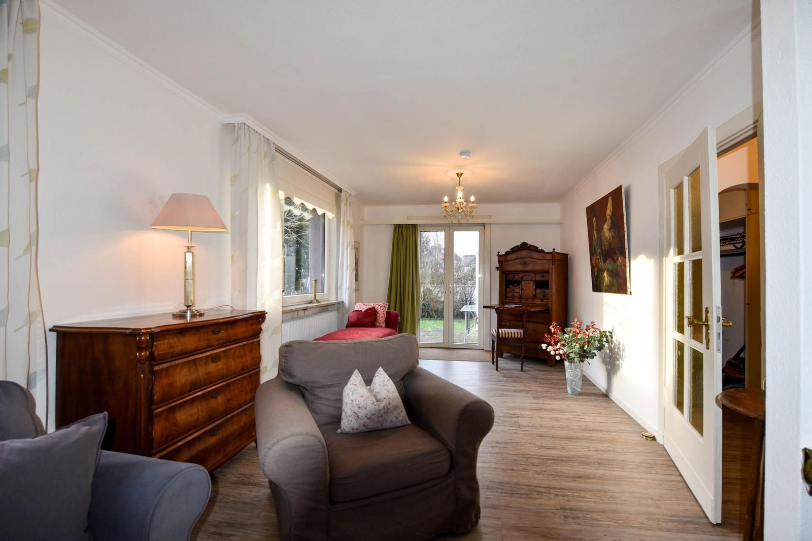 Wohnzimmer mit Sessel, Schrank und Türen zum Garten.