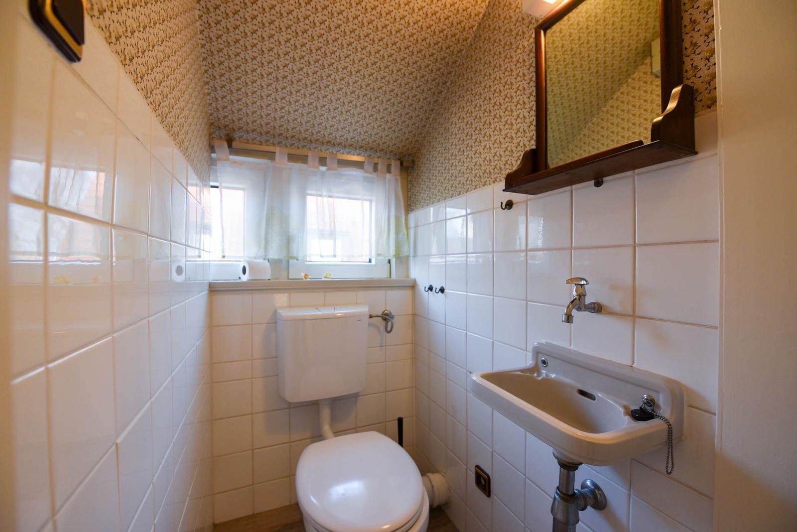 Badezimmer mit Toilette, Waschbecken und Fenster mit Vorhängen.