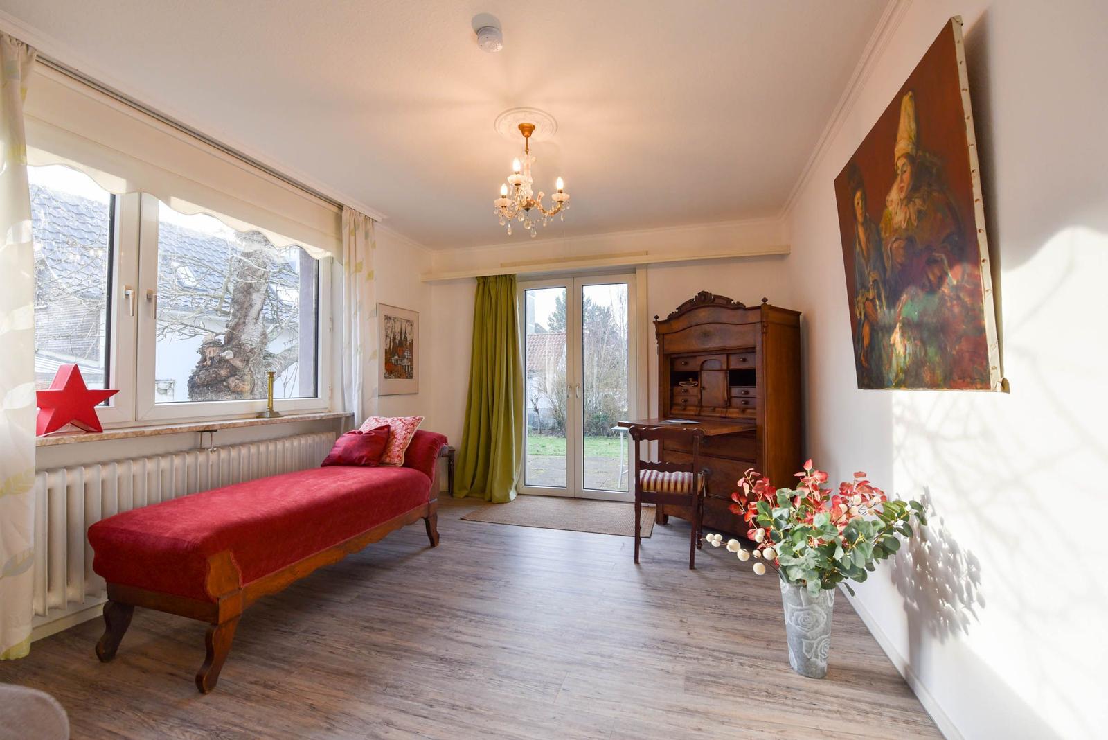 Ein Raum mit rotem Sofa, Holzboden und grünen Vorhängen vor der Glastür.