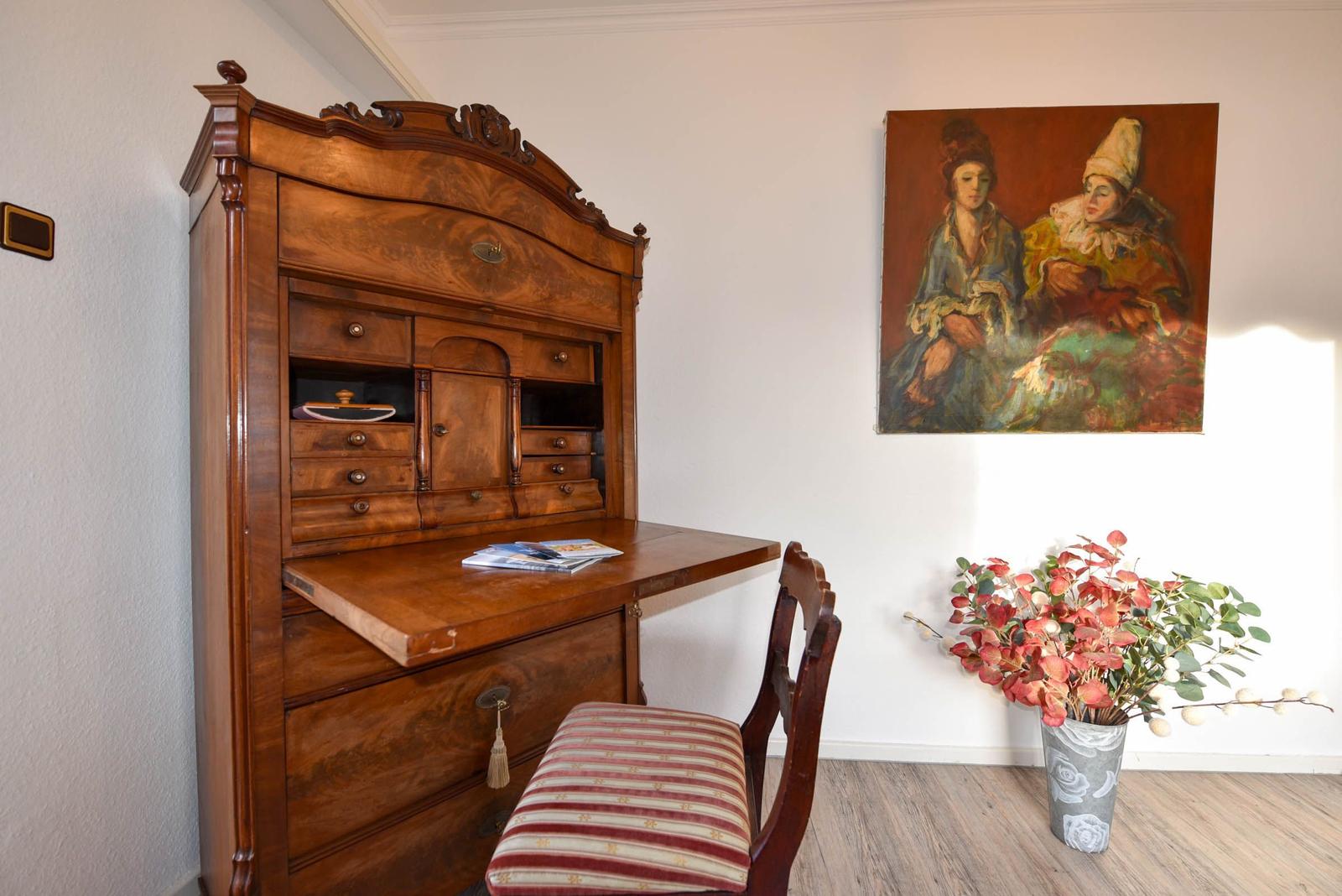 Antikschreibtisch mit Stuhl, Wandbild und Blumenarrangement im Raum.