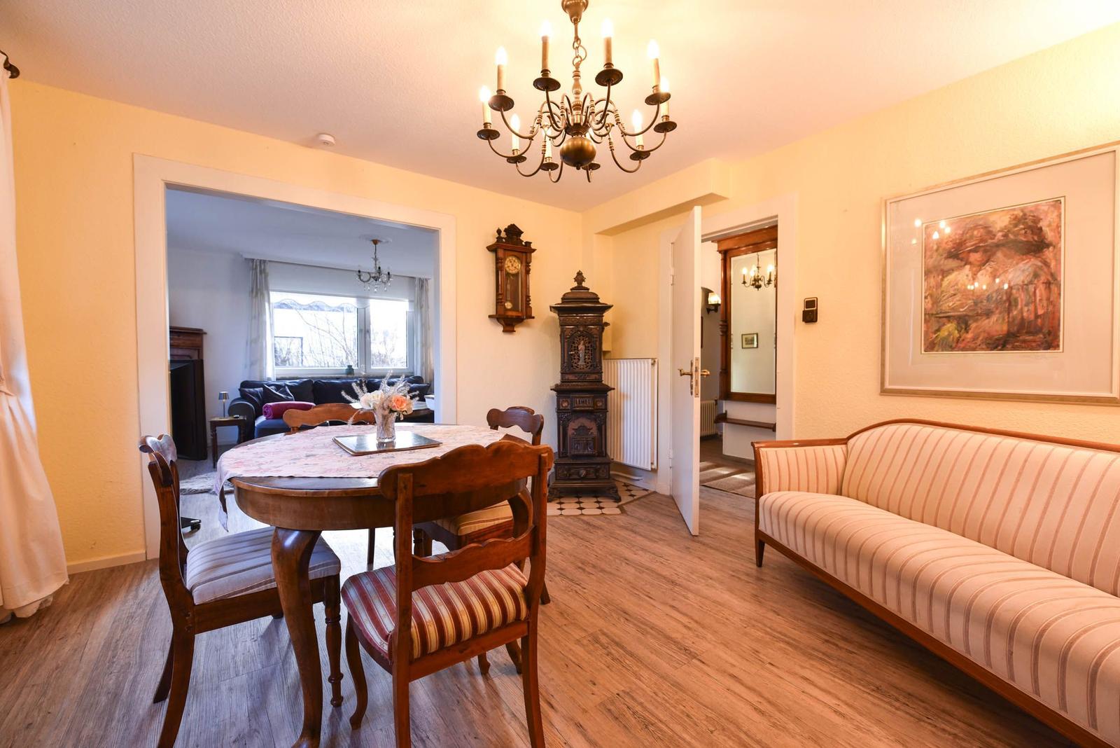 Esszimmer mit Holztisch, Stühlen und Sofa. Hintergrund: Wohnzimmer mit Kamin und Fenster.