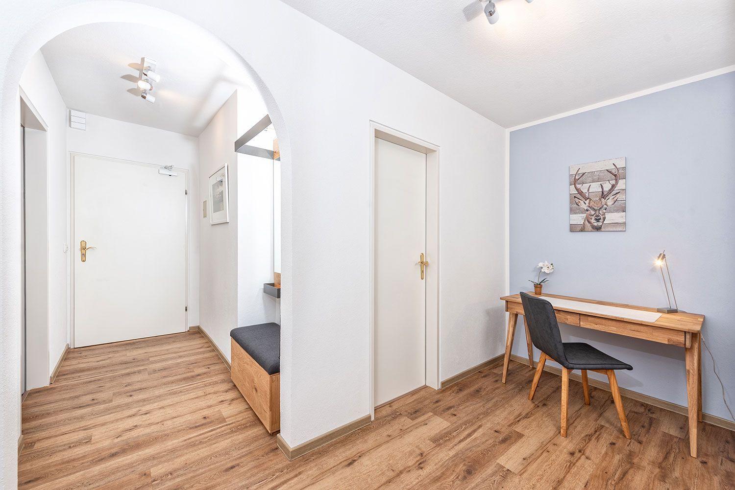 Flur mit Holzboden, Schreibtisch und Wandbild mit Hirsch. Türen und Bänke sind sichtbar.