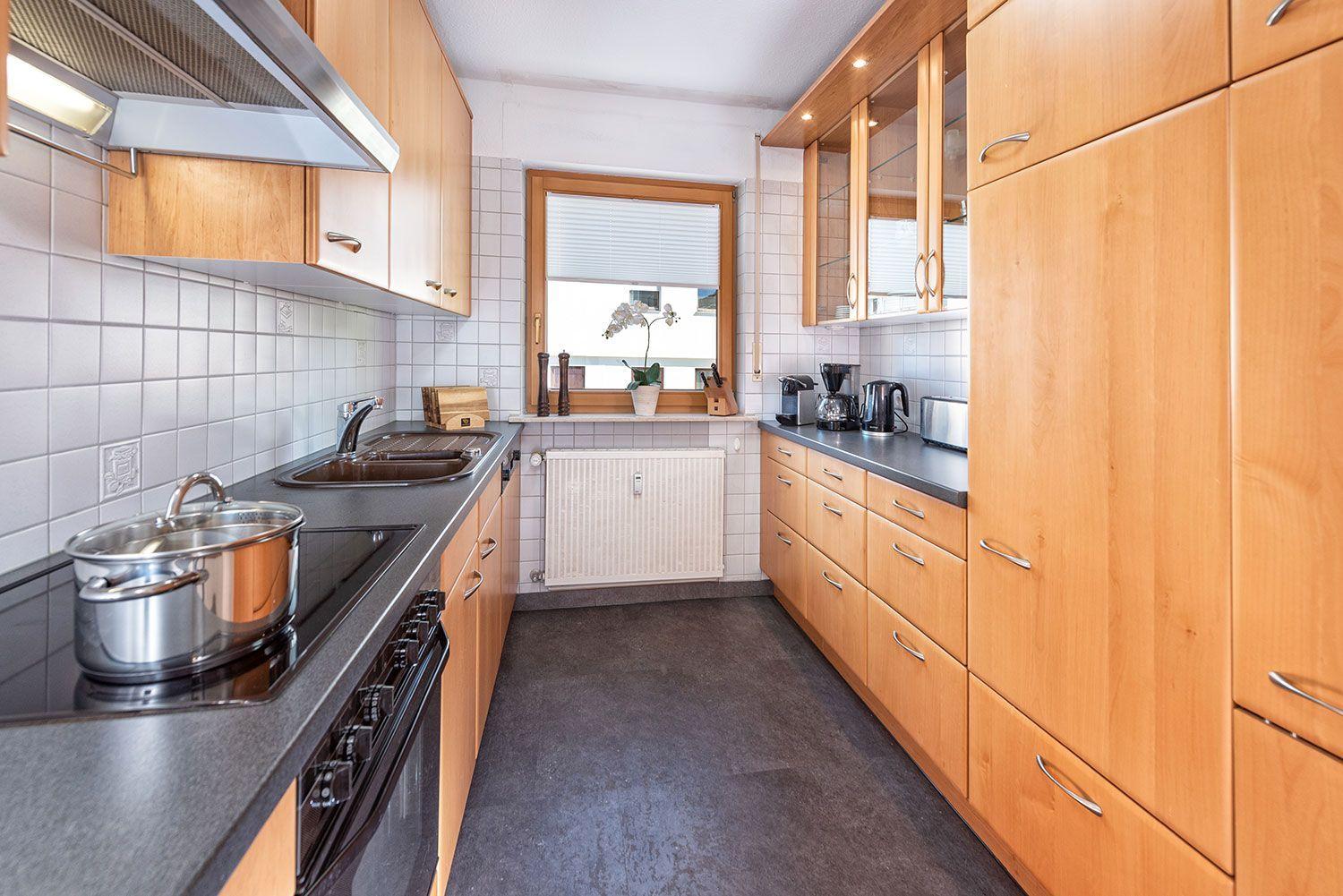 Küche mit Holzschränken, Edelstahlspüle und Fenster mit Pflanze.