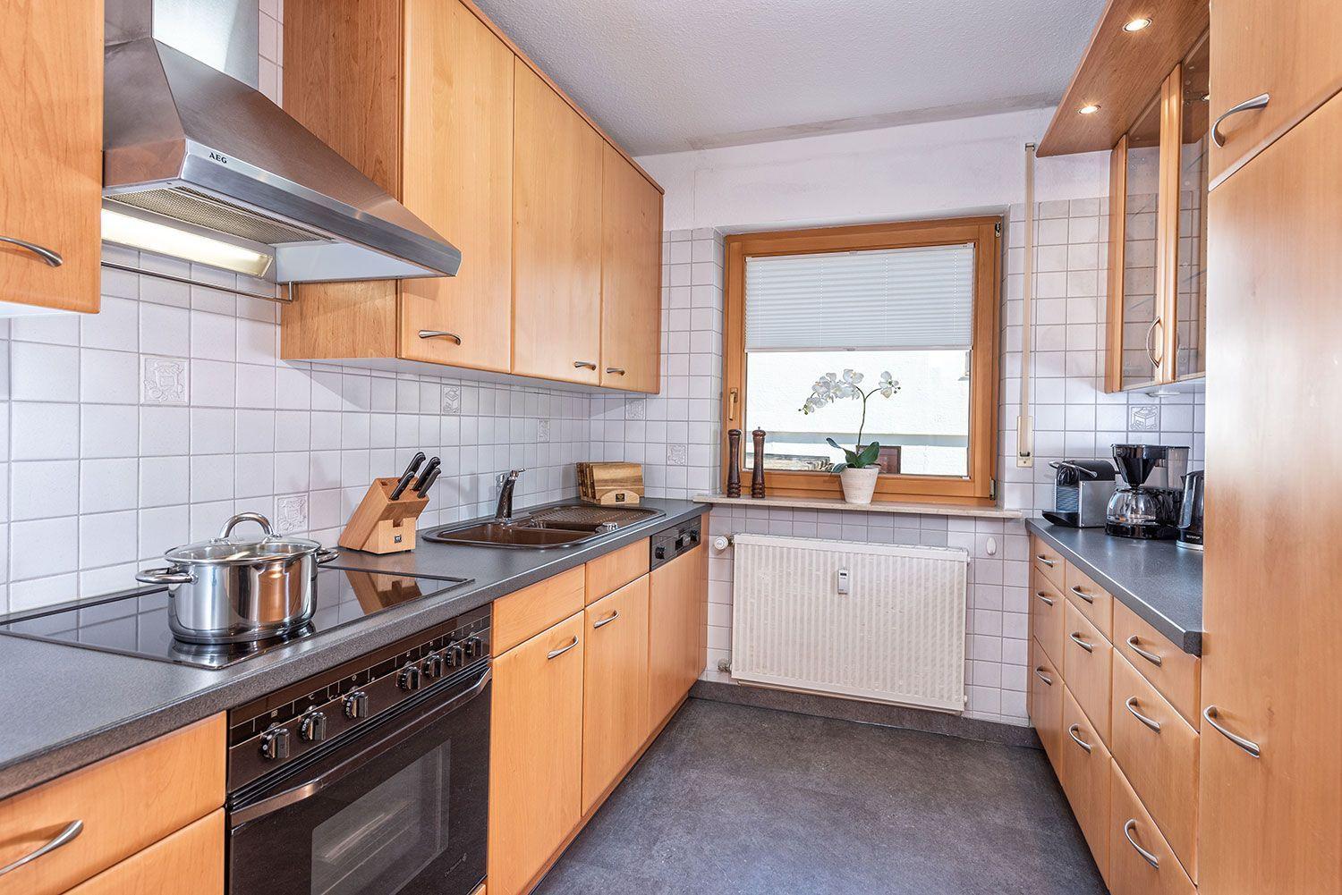 Küche mit Holzschränken, Edelstahlherd und Fenster mit Pflanze.