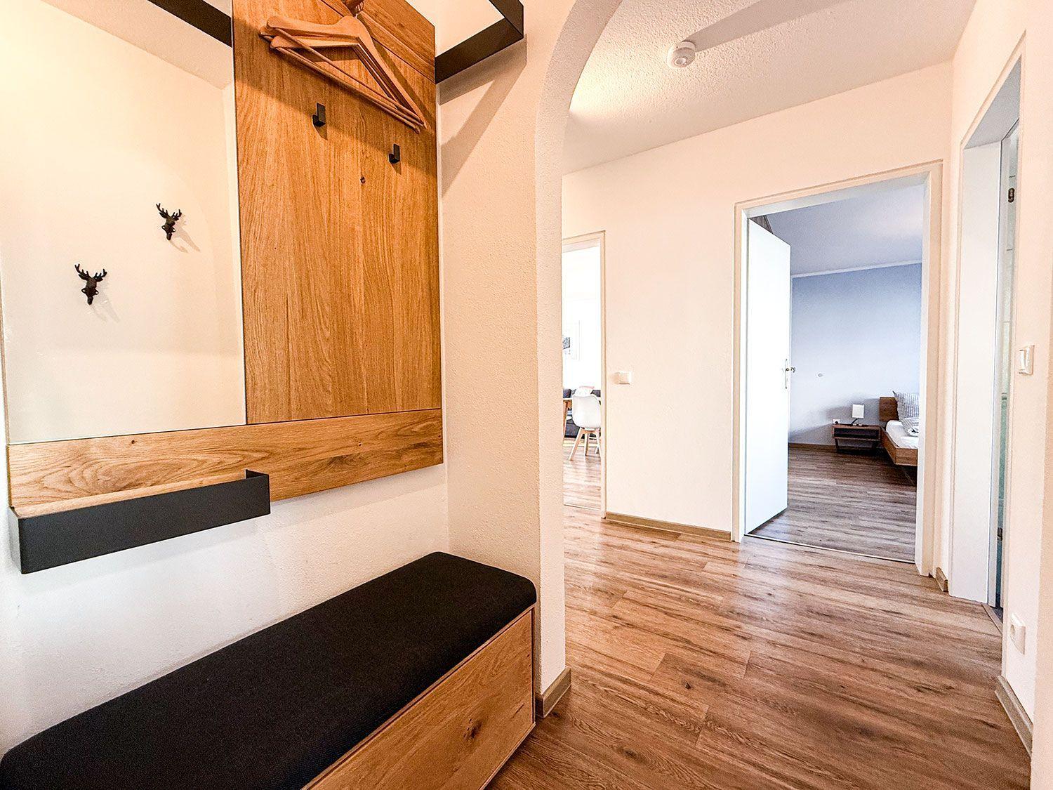 Eingangsbereich mit Holzgarderobe und Sitzbank. Durchgang zu Schlafzimmer und Wohnbereich.