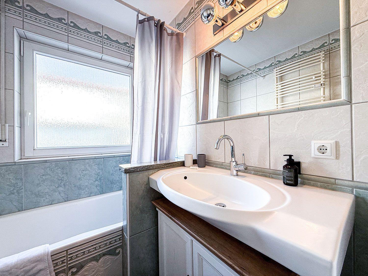 Bad mit Waschbecken, Spiegel und Badewanne mit Fenster.