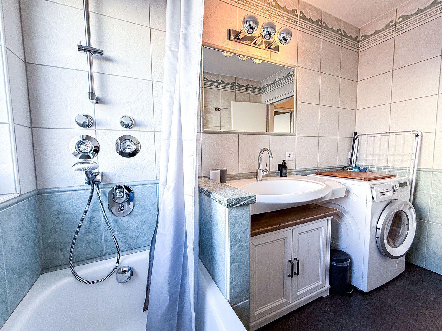 Bad mit Badewanne, Dusche, Waschbecken und Waschmaschine.