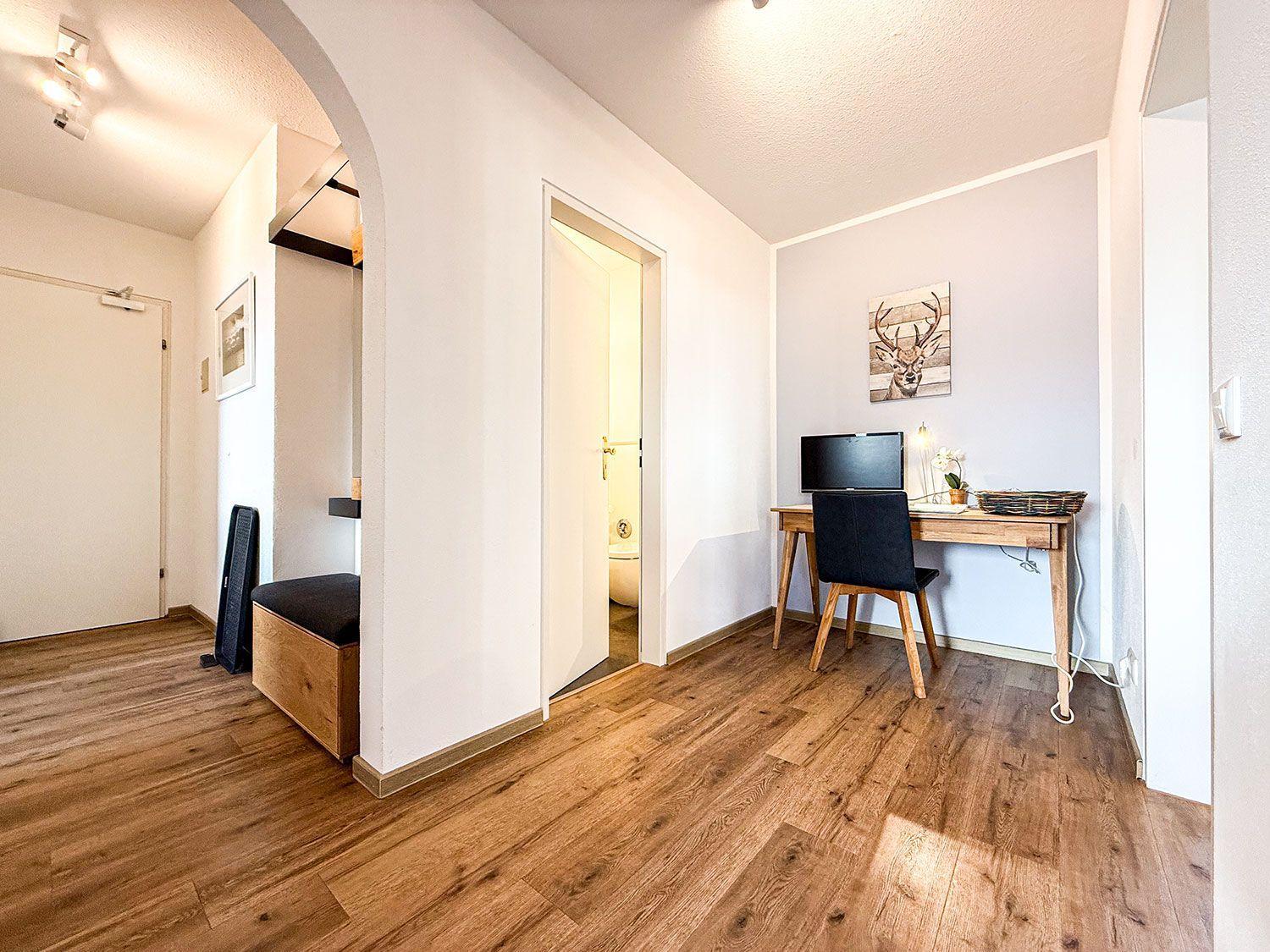 Ein Raum mit Holzboden, Schreibtisch, Stuhl und Wandbild eines Hirsches.