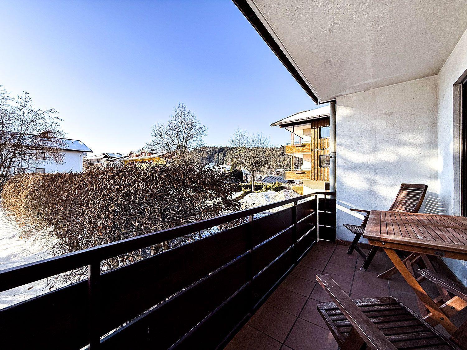 Terrasse mit Holztisch und Stühlen, Blick auf verschneite Landschaft und Gebäude.