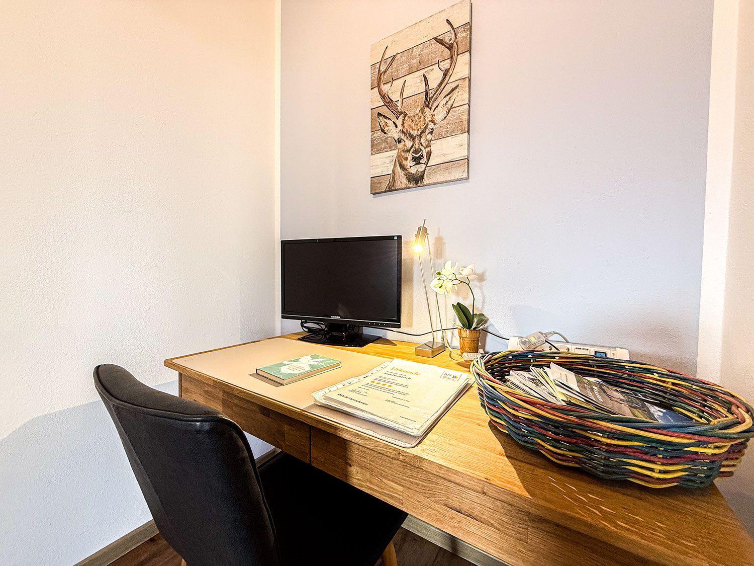Schreibtisch mit Monitor, Stuhl und Wandbild eines Hirsches.