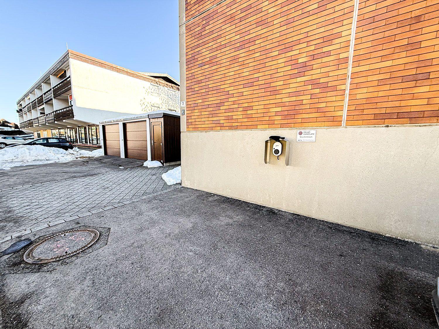Einfahrt mit Garagen und Schneehaufen vor einem Gebäude mit Backsteinfassade.