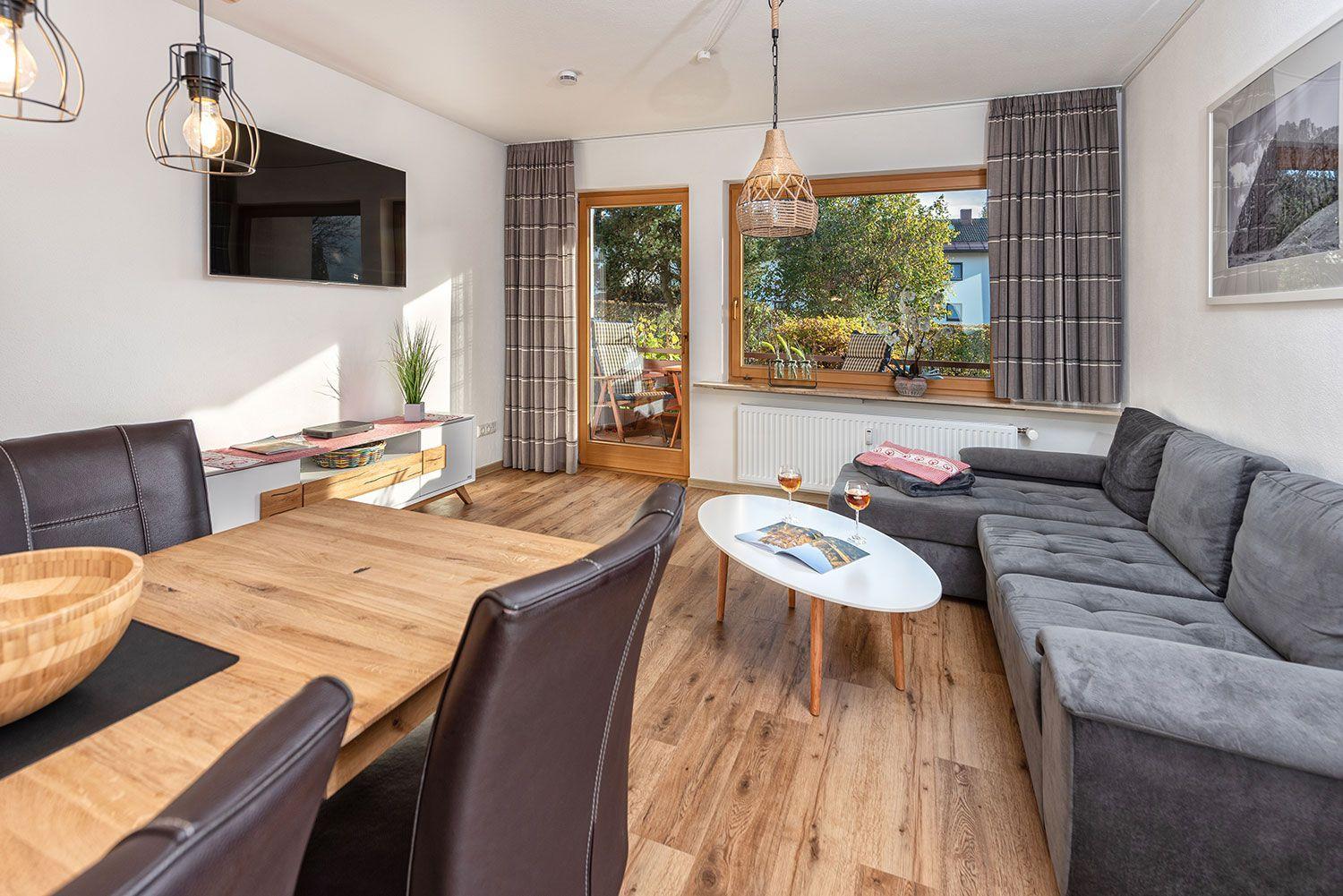 Wohn- und Essbereich mit Sofa, Tisch und TV. Durchgang zur Terrasse.