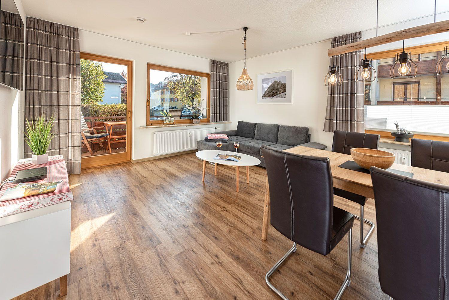 Wohn- und Essbereich mit Holzboden, Sofa, Esstisch und Blick auf Balkon.