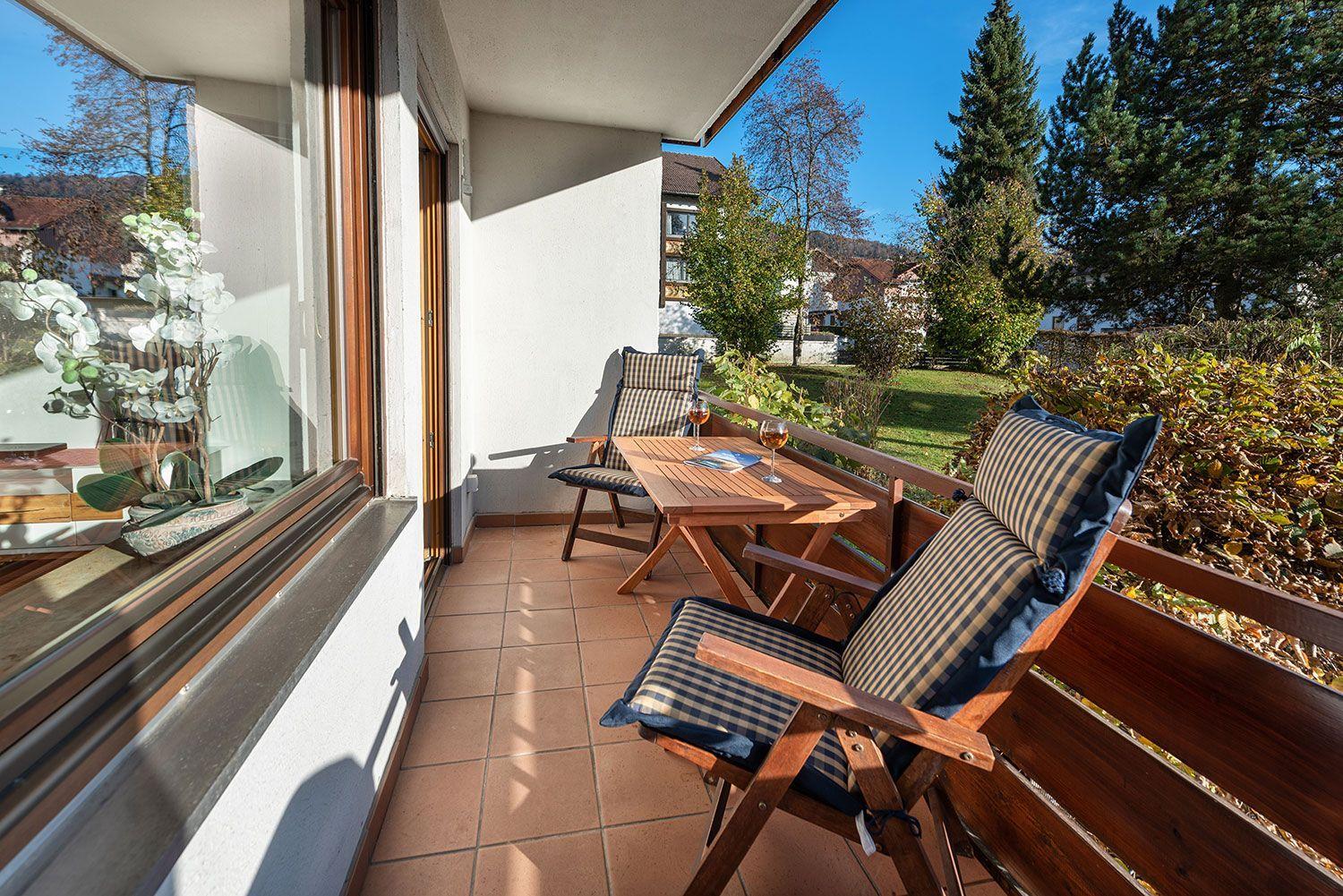 Terrasse mit Holztisch, zwei Stühlen und Blick auf grünen Garten.