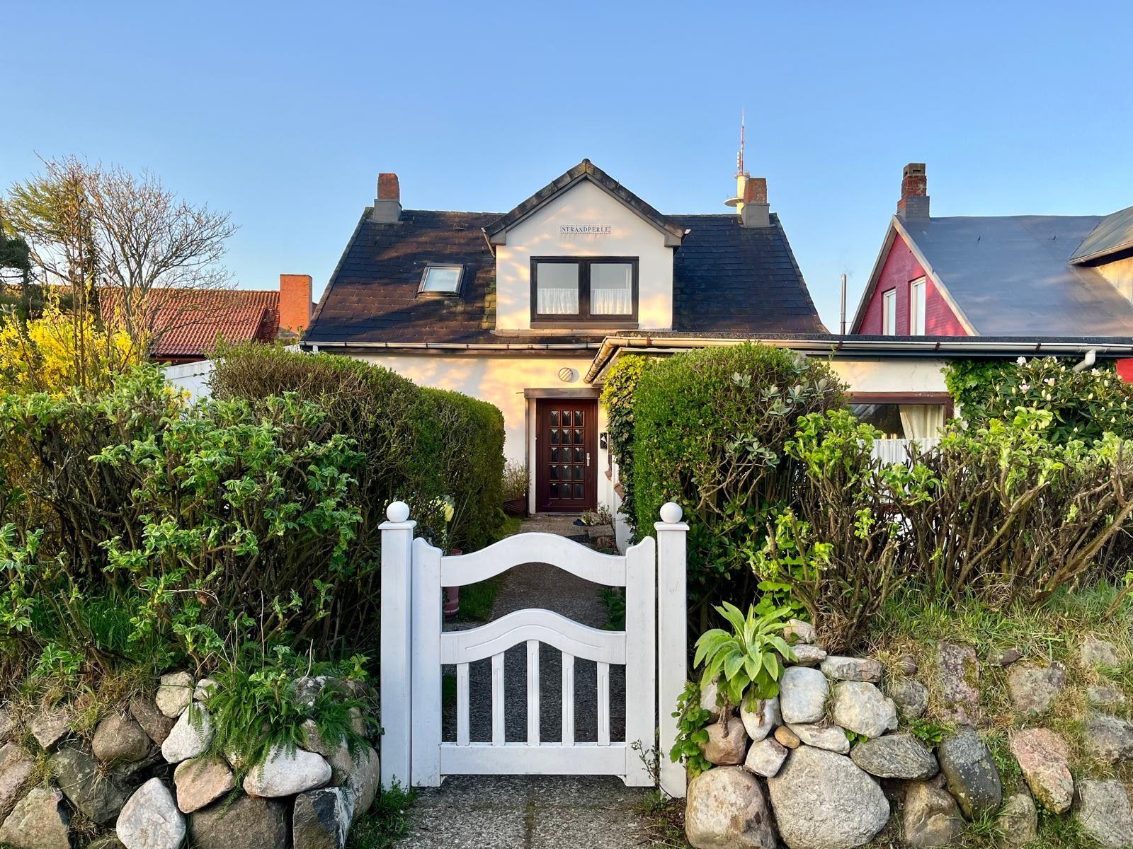 Haus mit weißem Tor und grünen Hecken im Vordergrund.