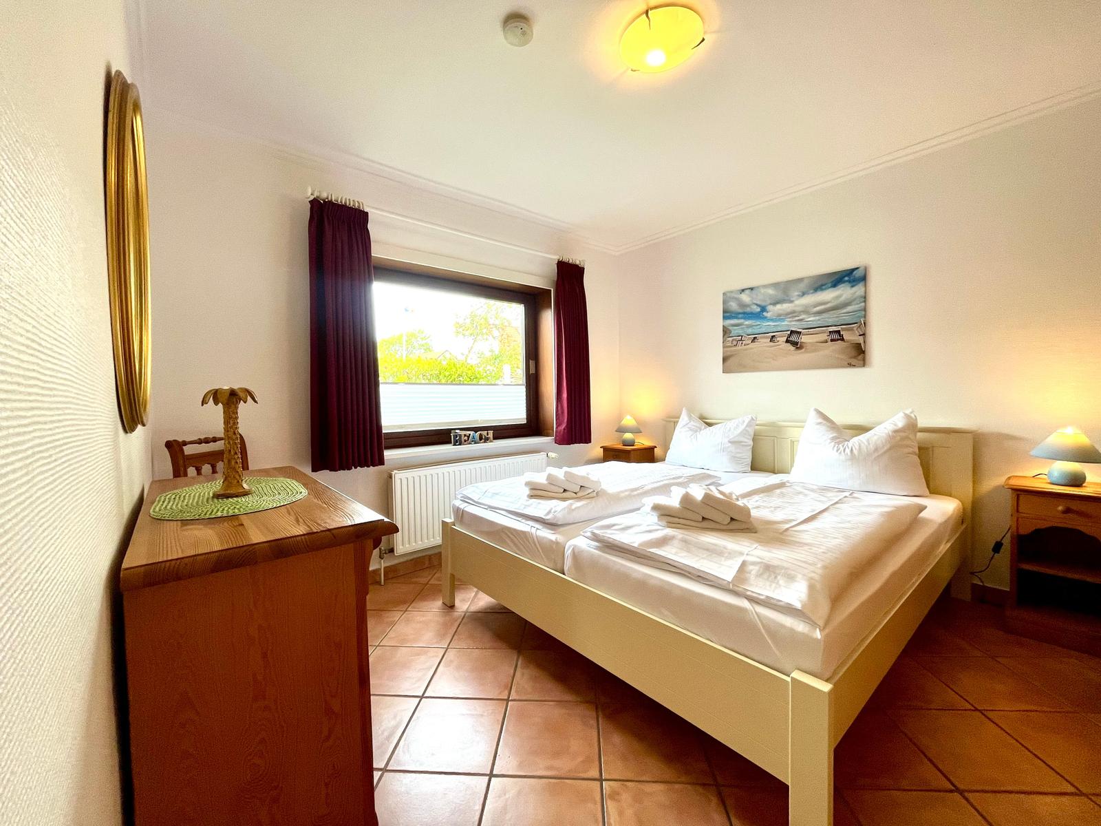 Schlafzimmer mit Doppelbett, Fenster, Nachttischen und Wandbild.