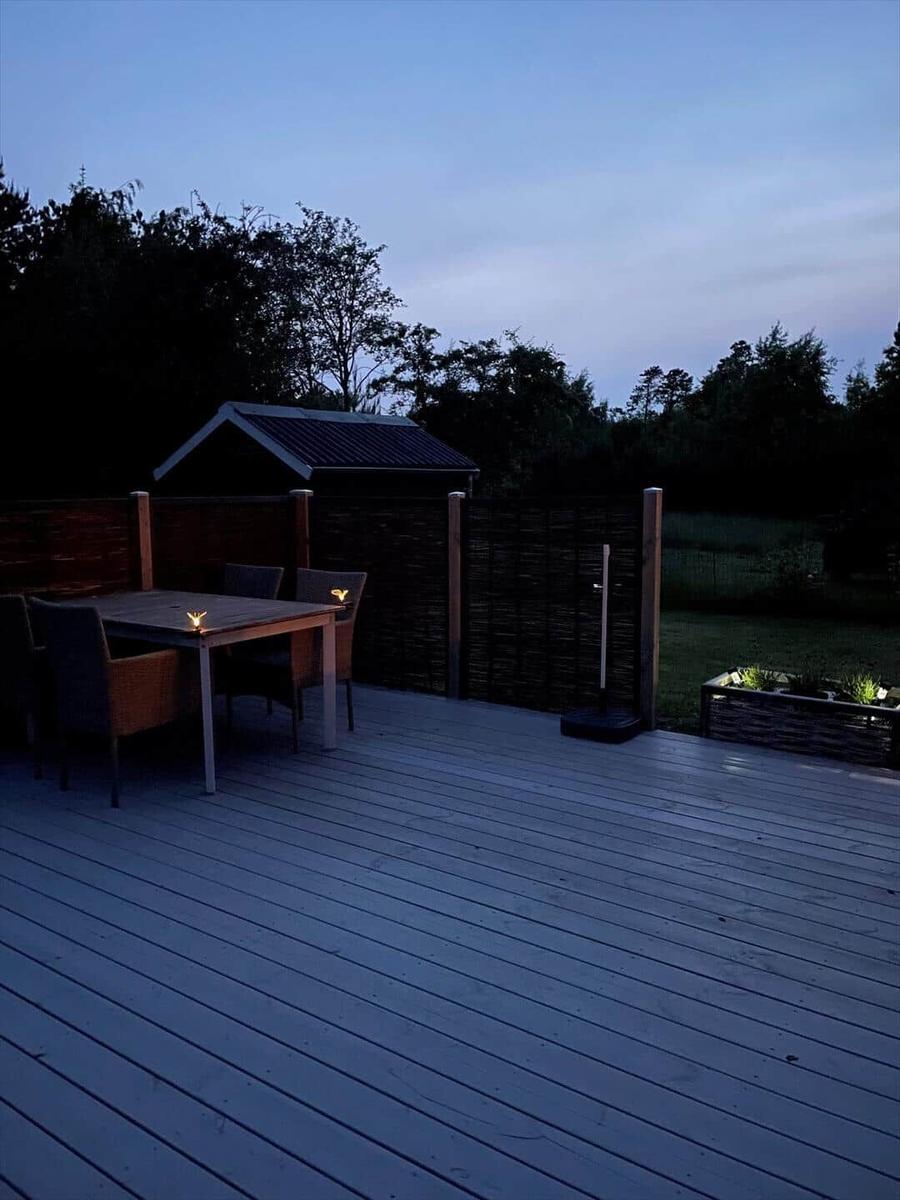 Terrasse mit Tisch, Stühlen und Gartenzaun bei Dämmerung.