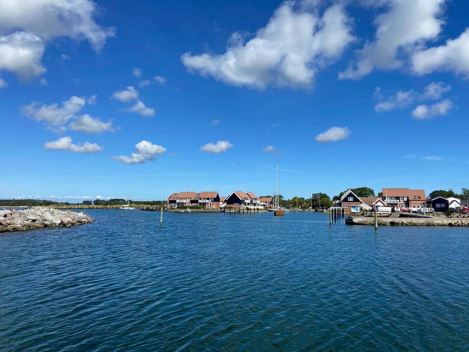 Hafen mit Booten und Häusern unter blauem Himmel mit weißen Wolken.