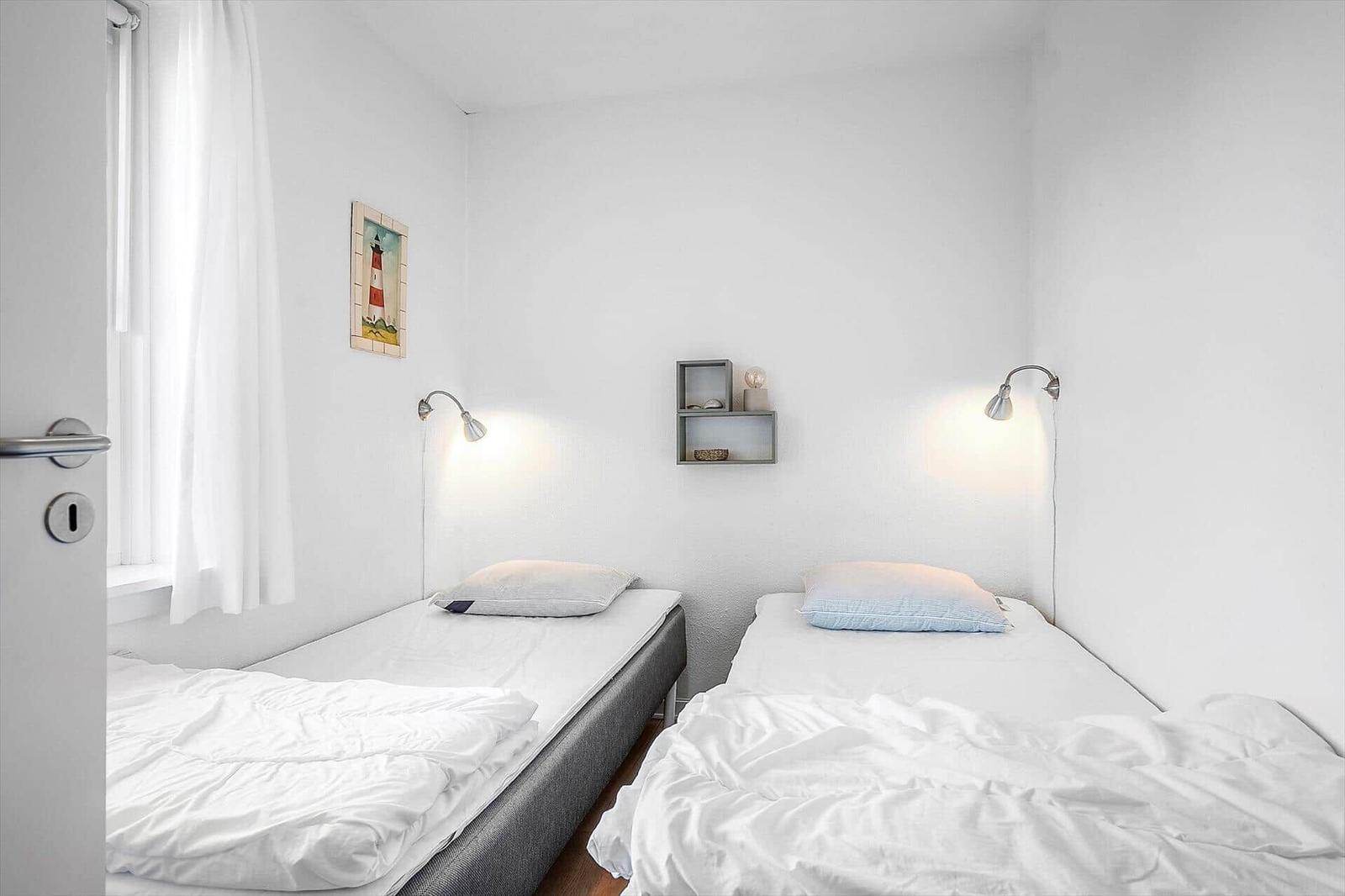 Zwei Einzelbetten mit weißen Laken und Wandlampen in einem hellen Raum.