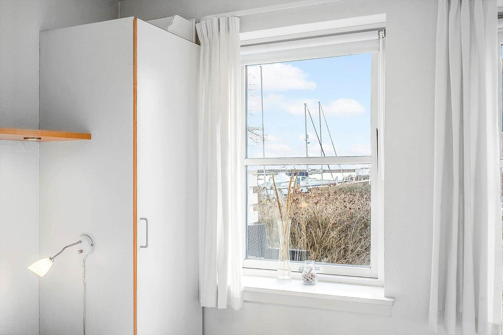 Ein Fenster mit Blick auf einen Hafen. Weiße Vorhänge und ein Schrank sind sichtbar.