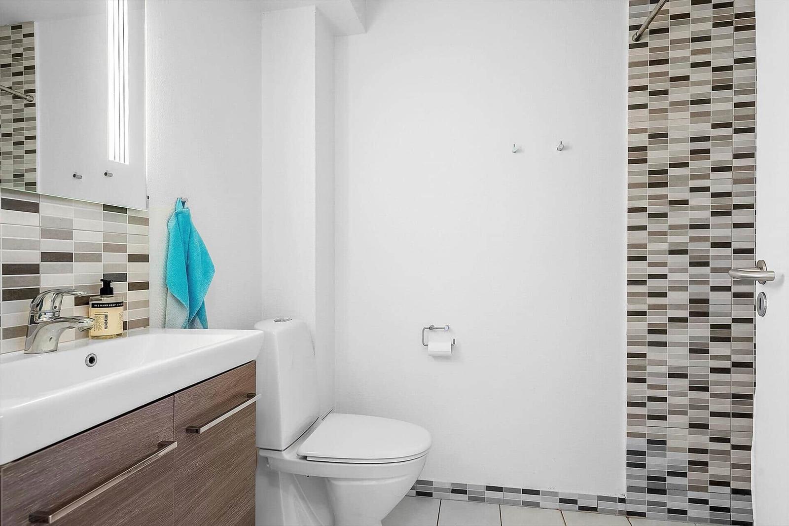 Badezimmer mit Waschbecken, Toilette und Dusche mit Mosaikfliesen.