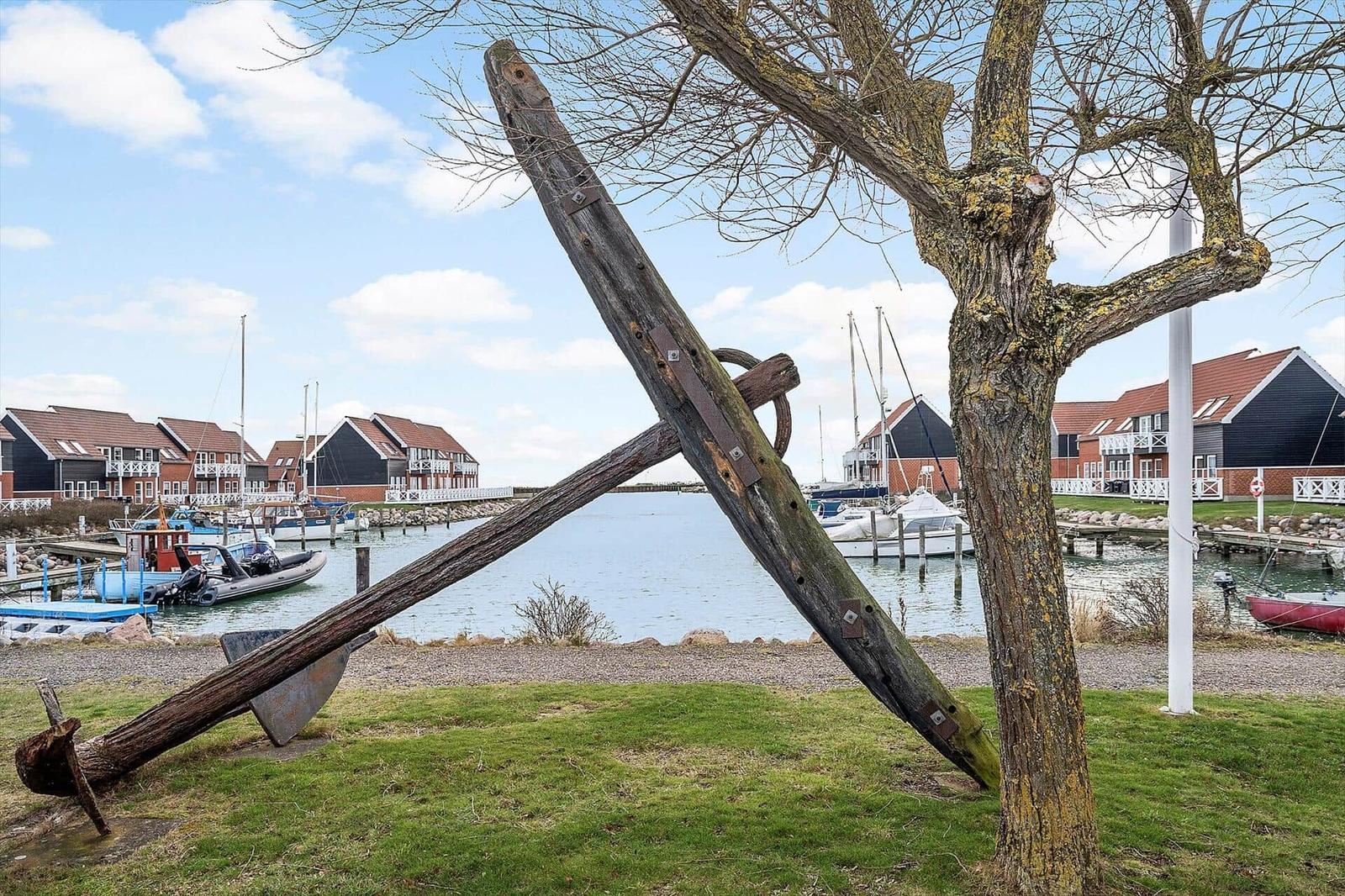 Großer Holzanker vor einem Hafen mit Booten und Häusern.