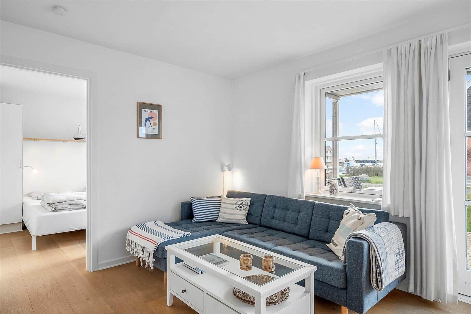 Wohnzimmer mit Sofa, Couchtisch und Blick auf Hafen. Schlafzimmer ist angrenzend.