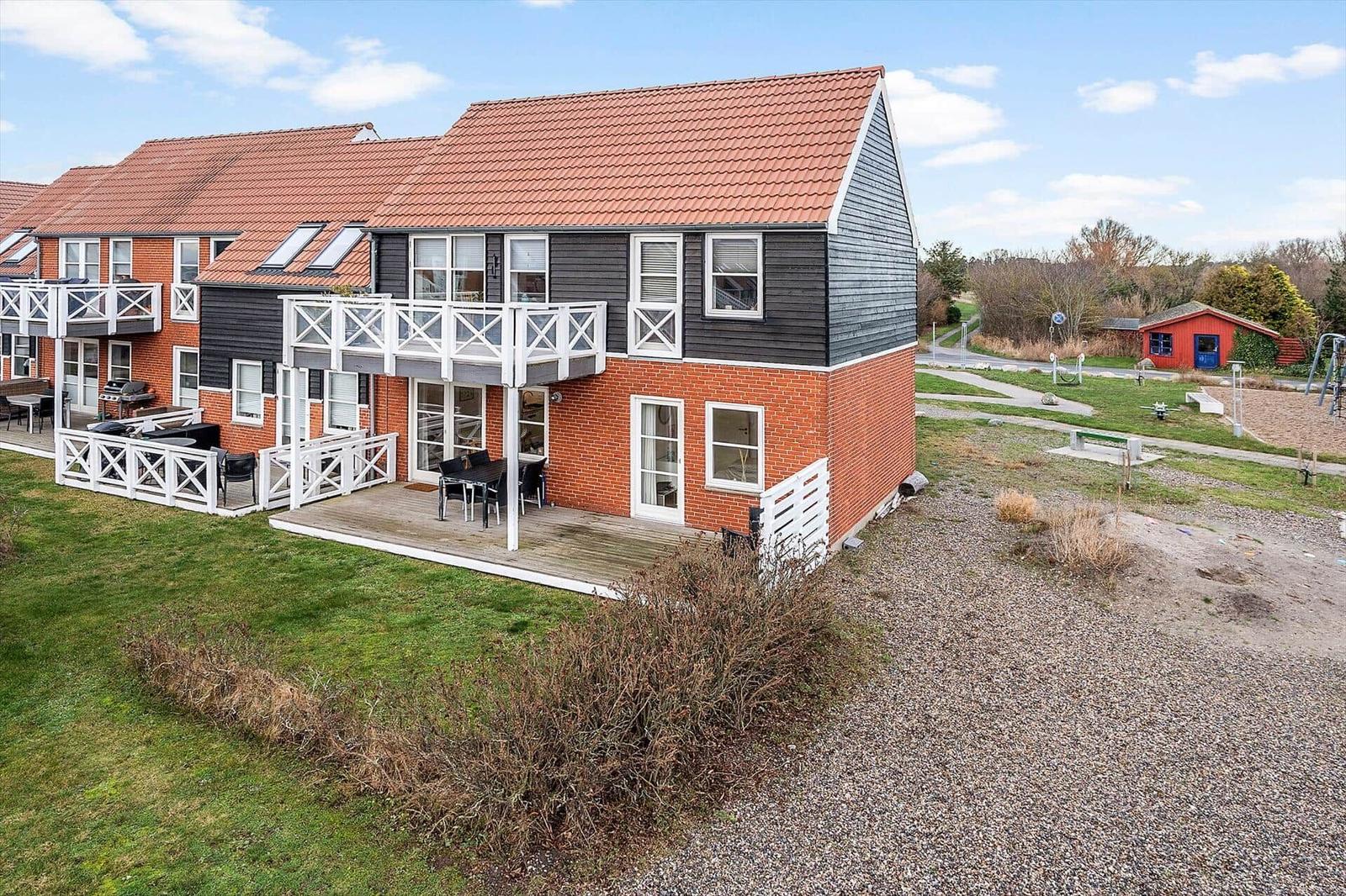 Zweistöckiges Ferienhaus mit Balkon, Terrasse und Garten. Rotes Dach und weiße Geländer.