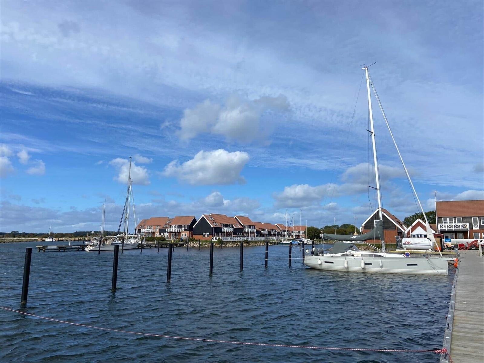 Segelyacht liegt im Hafen vor modernen Häusern mit roten Dächern.