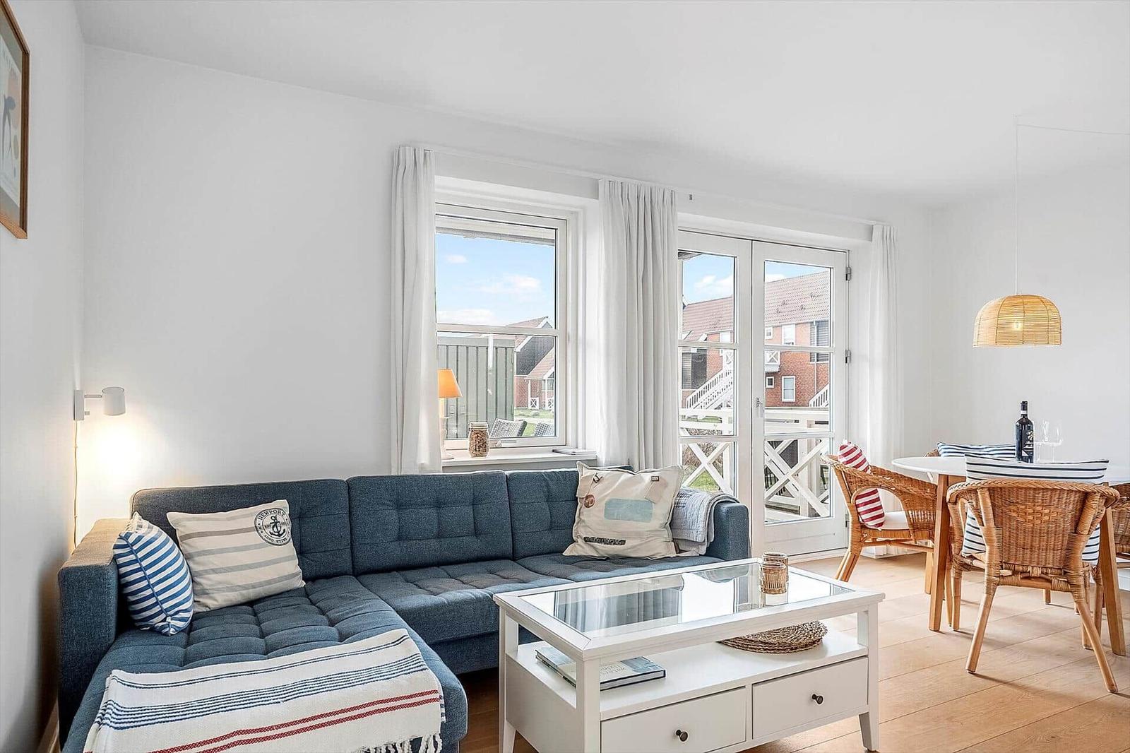 Ein Wohn- und Essbereich mit Sofa, Tisch und Stühlen. Durchgänge zu einer Terrasse.