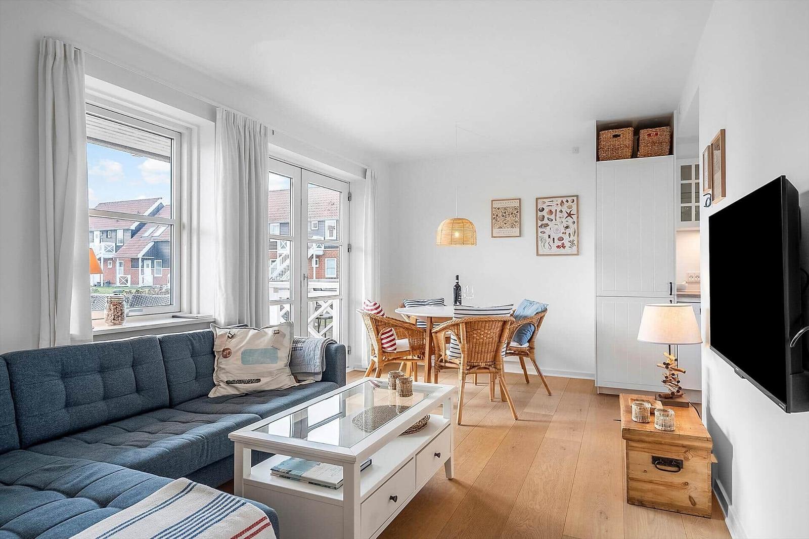 Wohn- und Essbereich mit Sofa, Tisch und TV. Durchgänge zu Balkon und Küche.