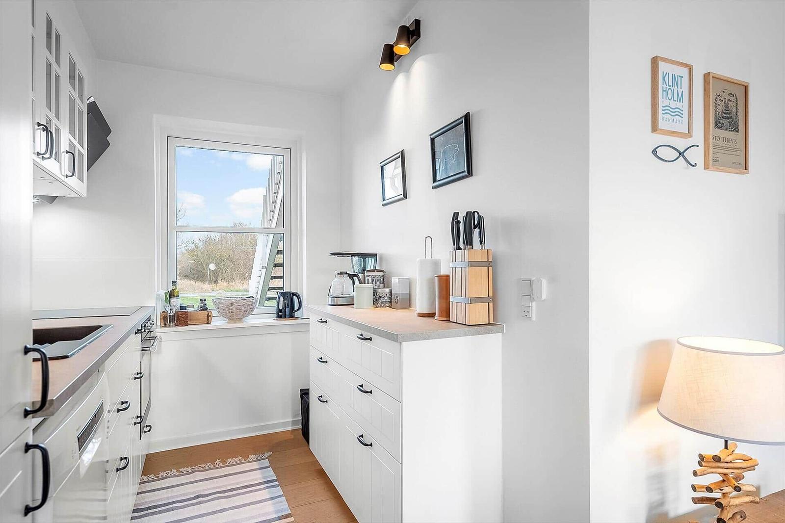 Küche mit Fenster, weißen Schränken und Küchenutensilien an der Wand.