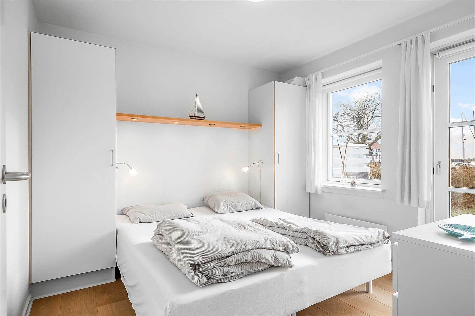 Schlafzimmer mit Bett, weißen Schränken und Fensterblick.