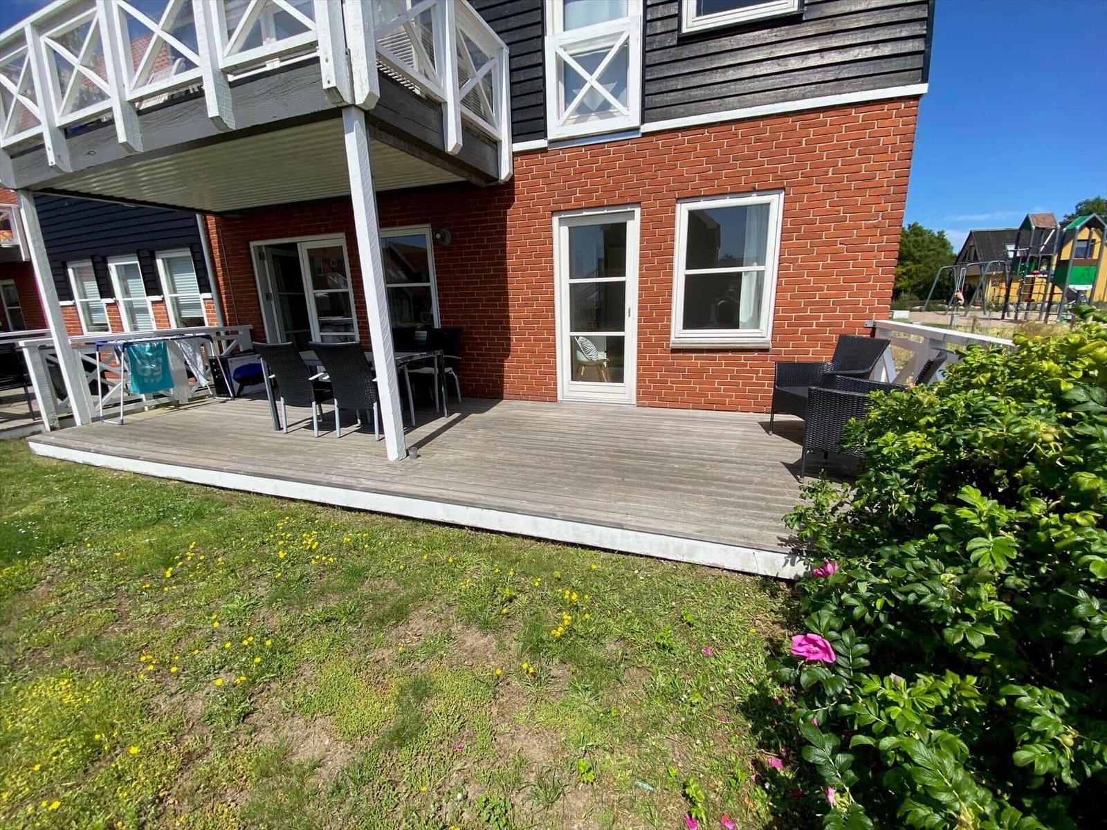 Haus mit Terrasse, Garten und Gartenmöbeln unter blauem Himmel.