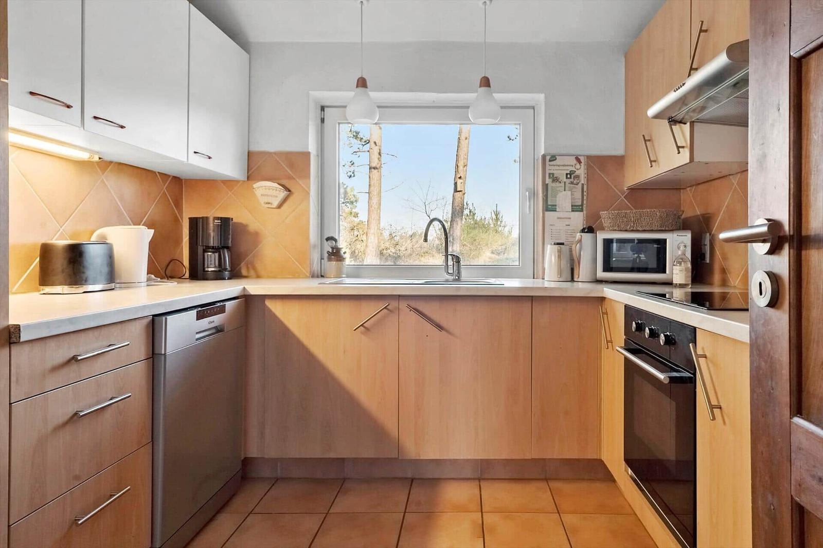 Küche mit Holzschränken, Spüle und Fensterblick auf Bäume