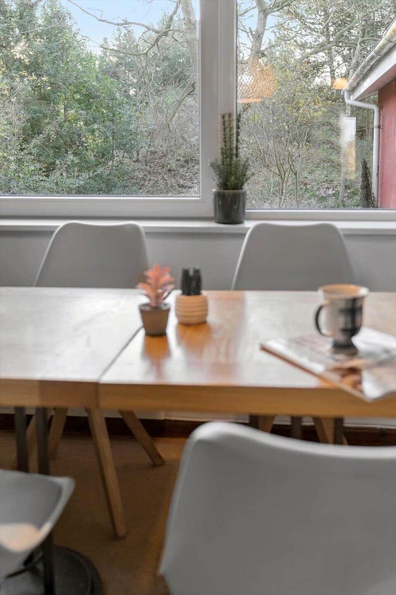 Esstisch mit Stühlen vor großem Fenster mit Blick auf Wald.