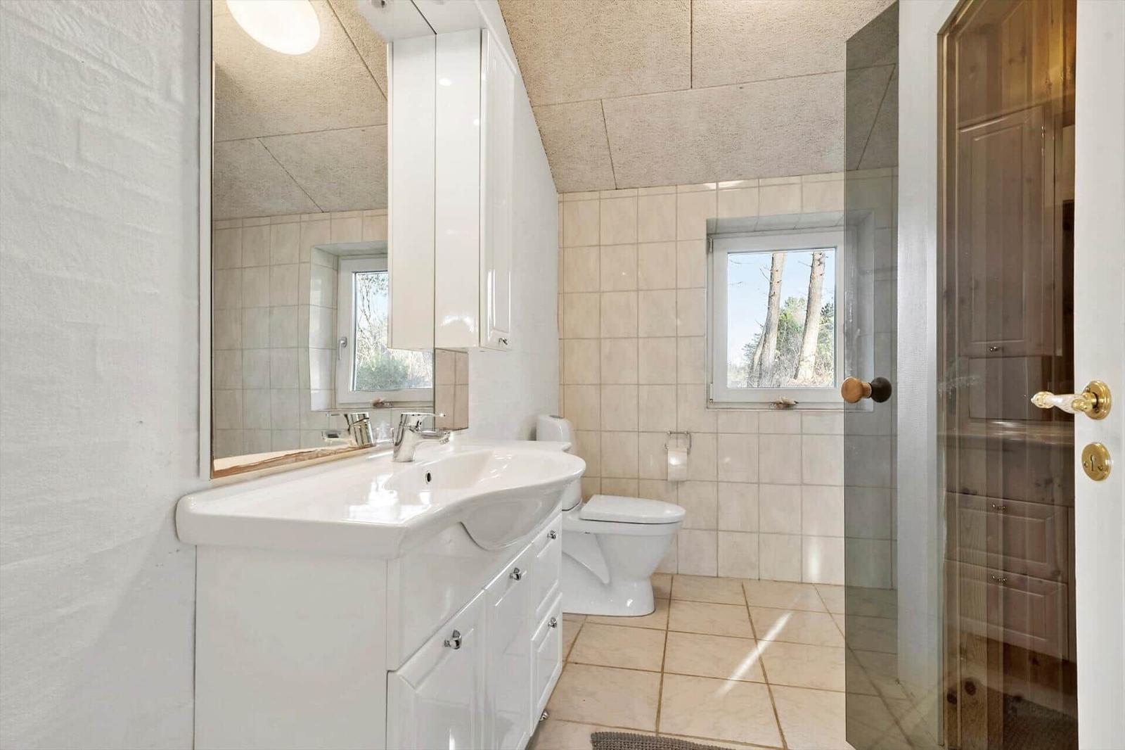 Badezimmer mit Waschbecken, Toilette und Dusche. Fenster mit Blick auf Bäume.