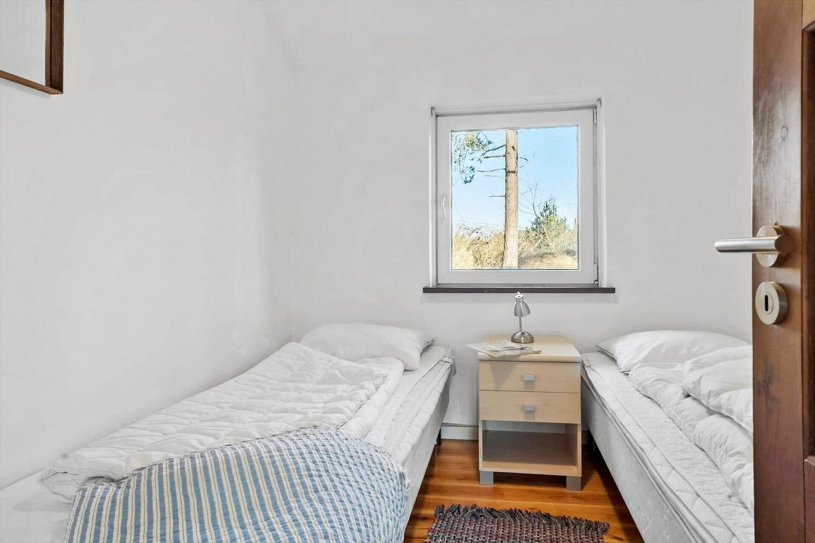 Zwei Einzelbetten, Nachttisch und Fenster mit Blick auf Bäume.