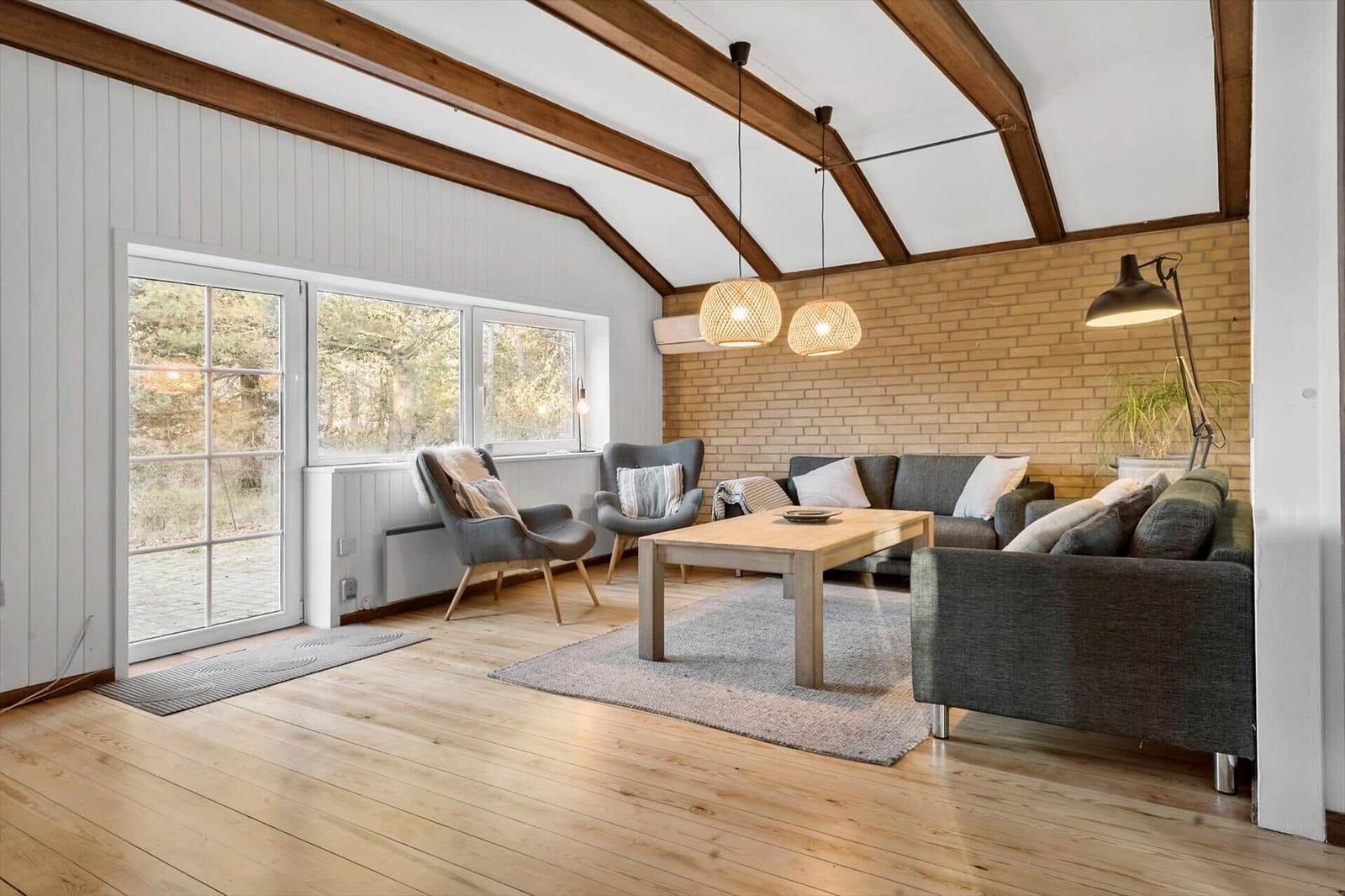 Wohnzimmer mit Holzboden, Sofa, Sessel und Fenster zur Außenseite.