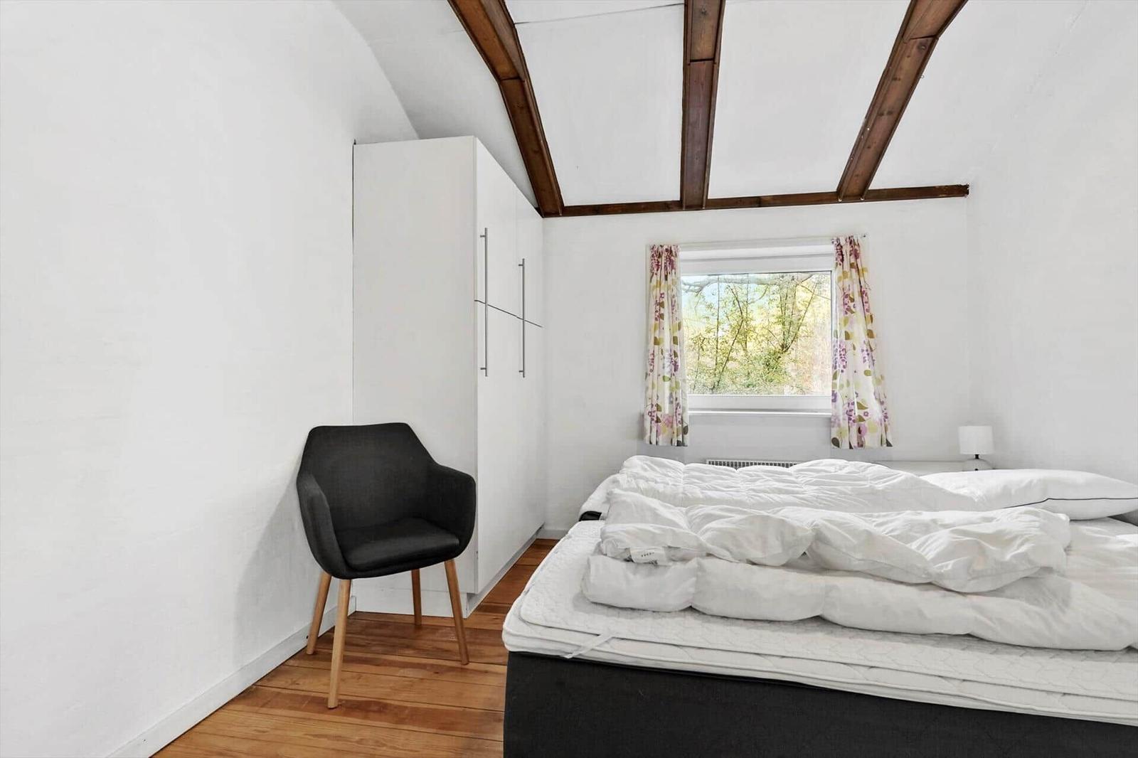 Schlafzimmer mit Bett, Stuhl und Fenster mit Vorhängen.