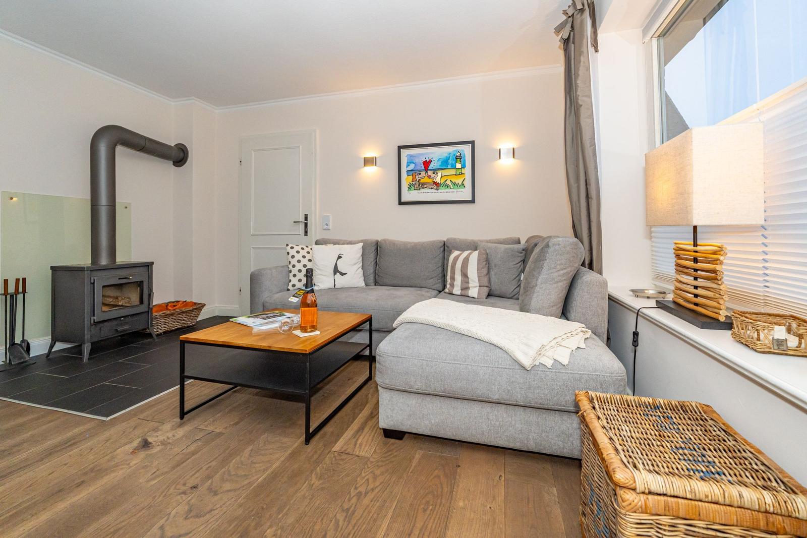 Wohnzimmer mit grauem Sofa, Holztisch und Kaminofen.