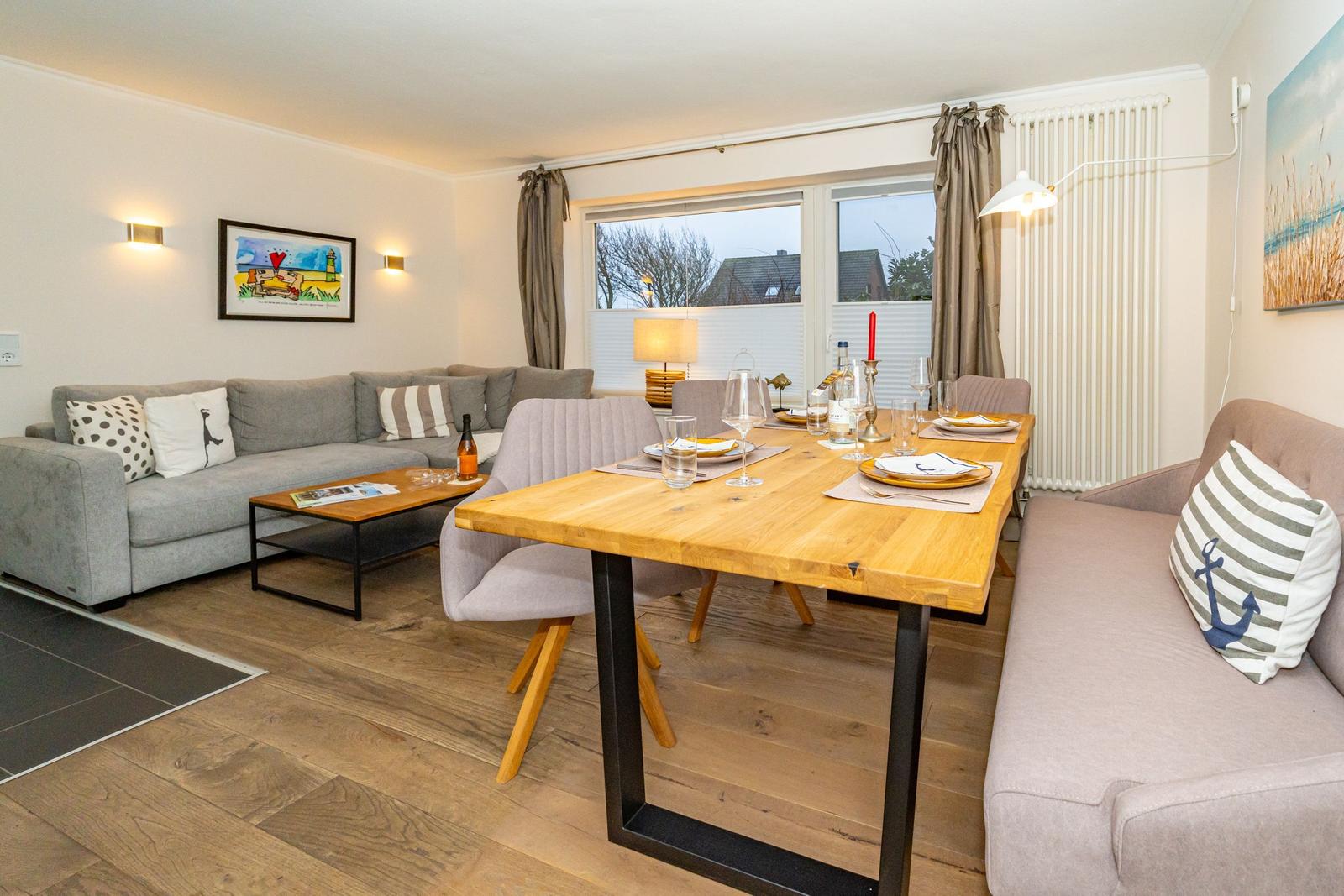 Wohn- und Essbereich mit Sofa, Tisch und Stühlen. Holzboden und Fenster mit Blick.