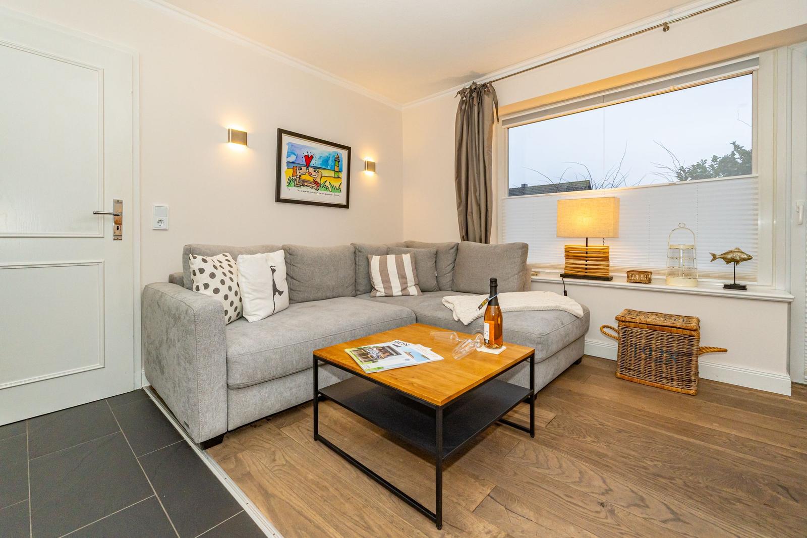 Wohnzimmer mit grauem Sofa, Holzfußboden und großem Fenster.