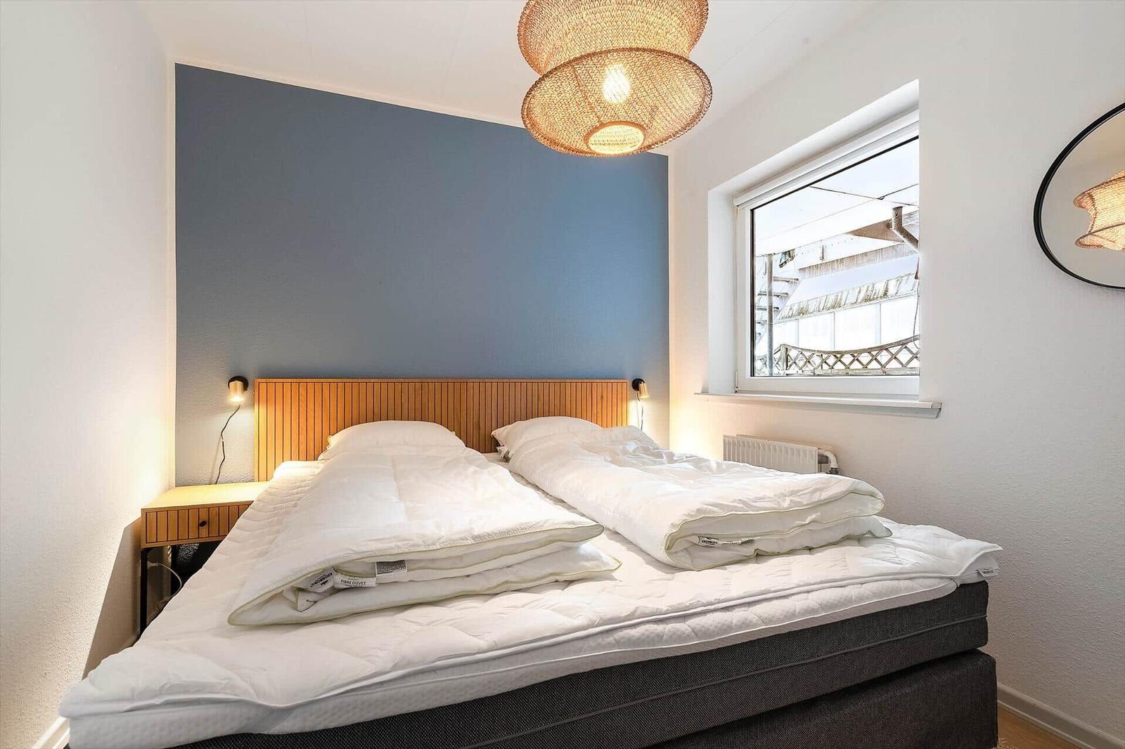 Schlafzimmer mit Doppelbett, blauer Wand und Fensterblick.