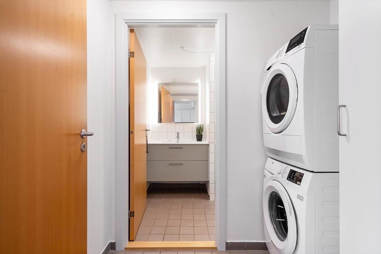 Waschraum mit Waschmaschine und Trockner. Blick in das Badezimmer mit Spiegel und Waschbecken.