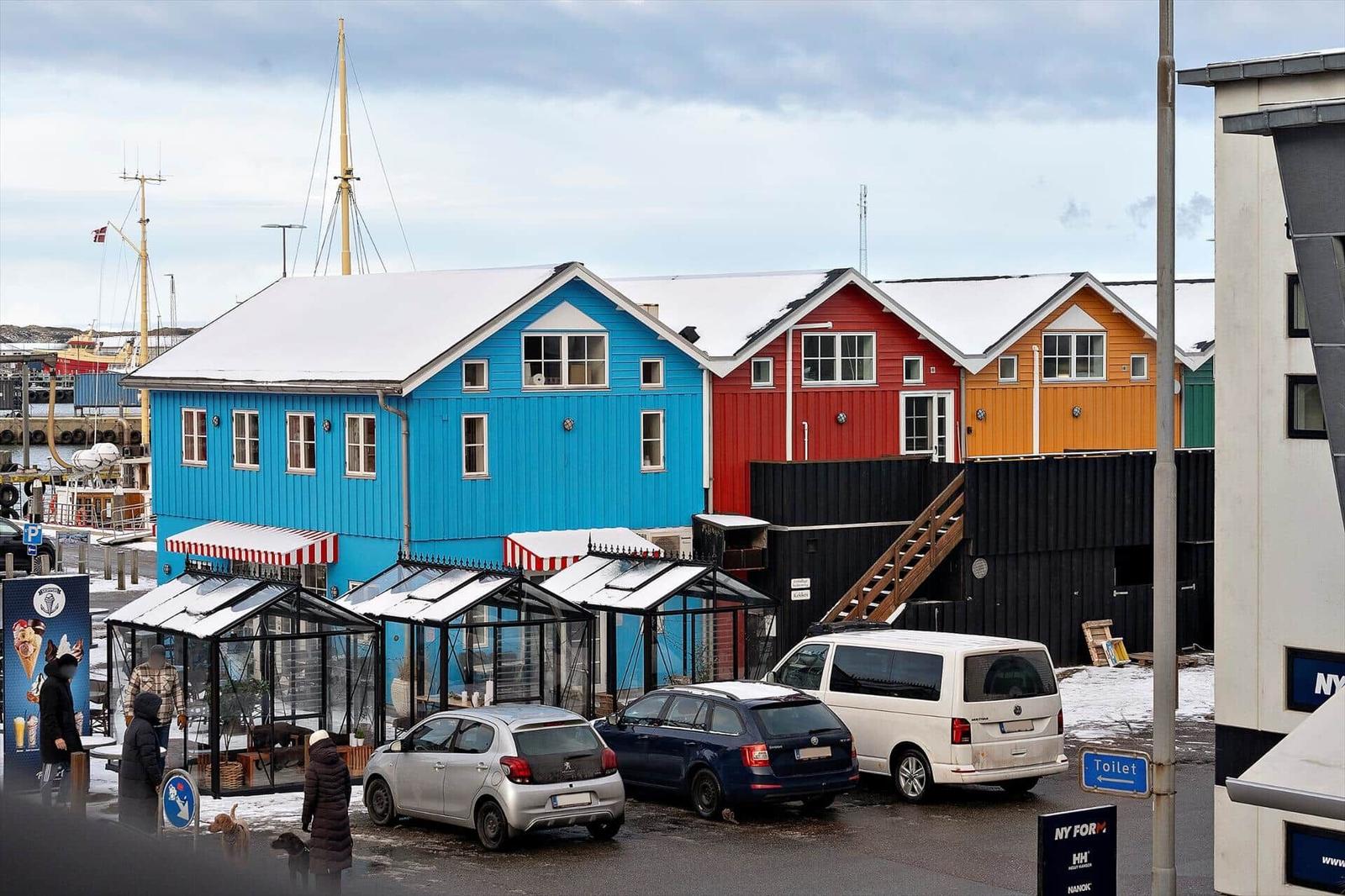 Farbige Häuser am Hafen mit Schnee auf Dächern und geparkten Autos.