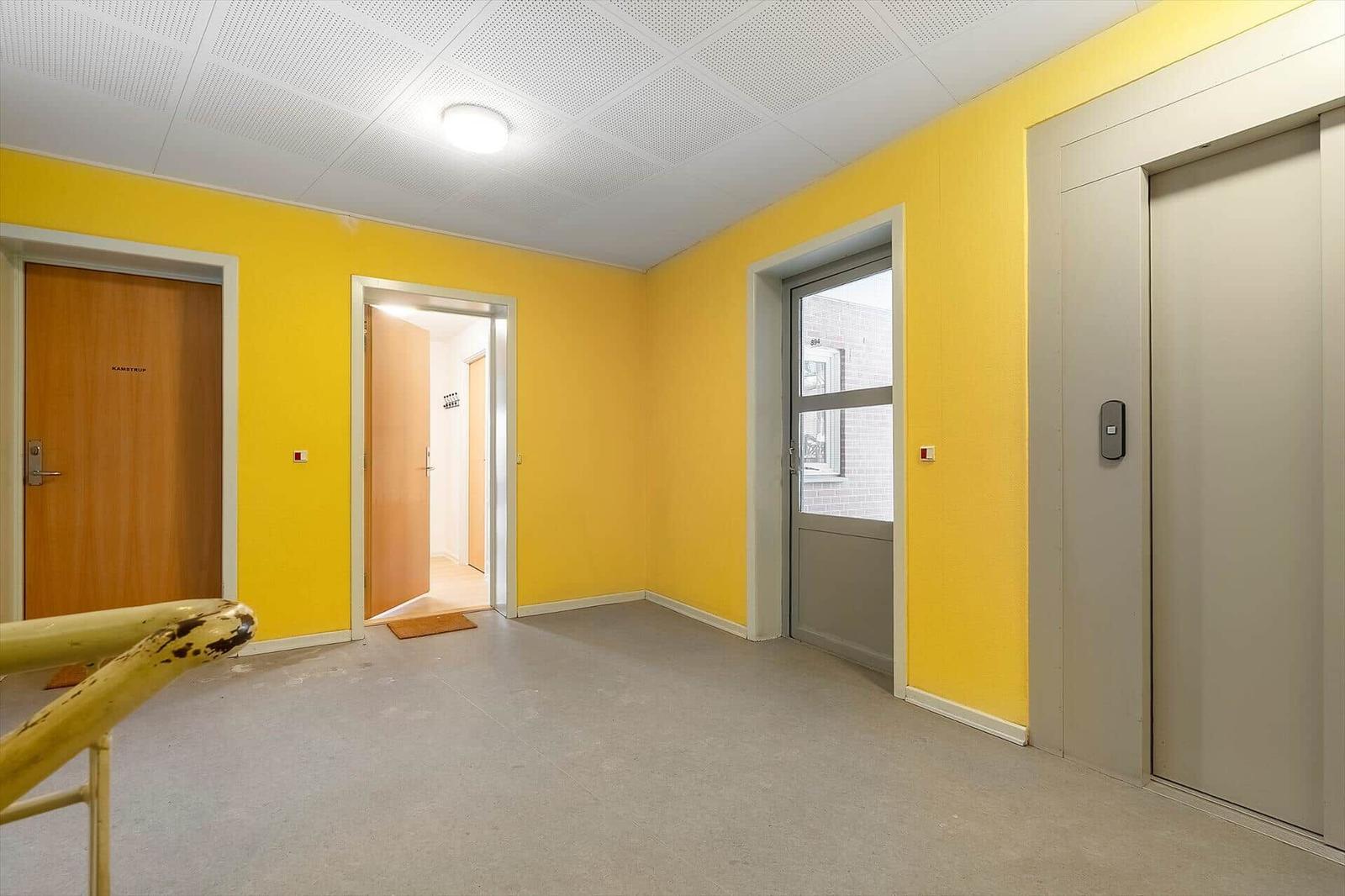 Flur mit gelben Wänden, Lift und Türen zu Wohnungen.