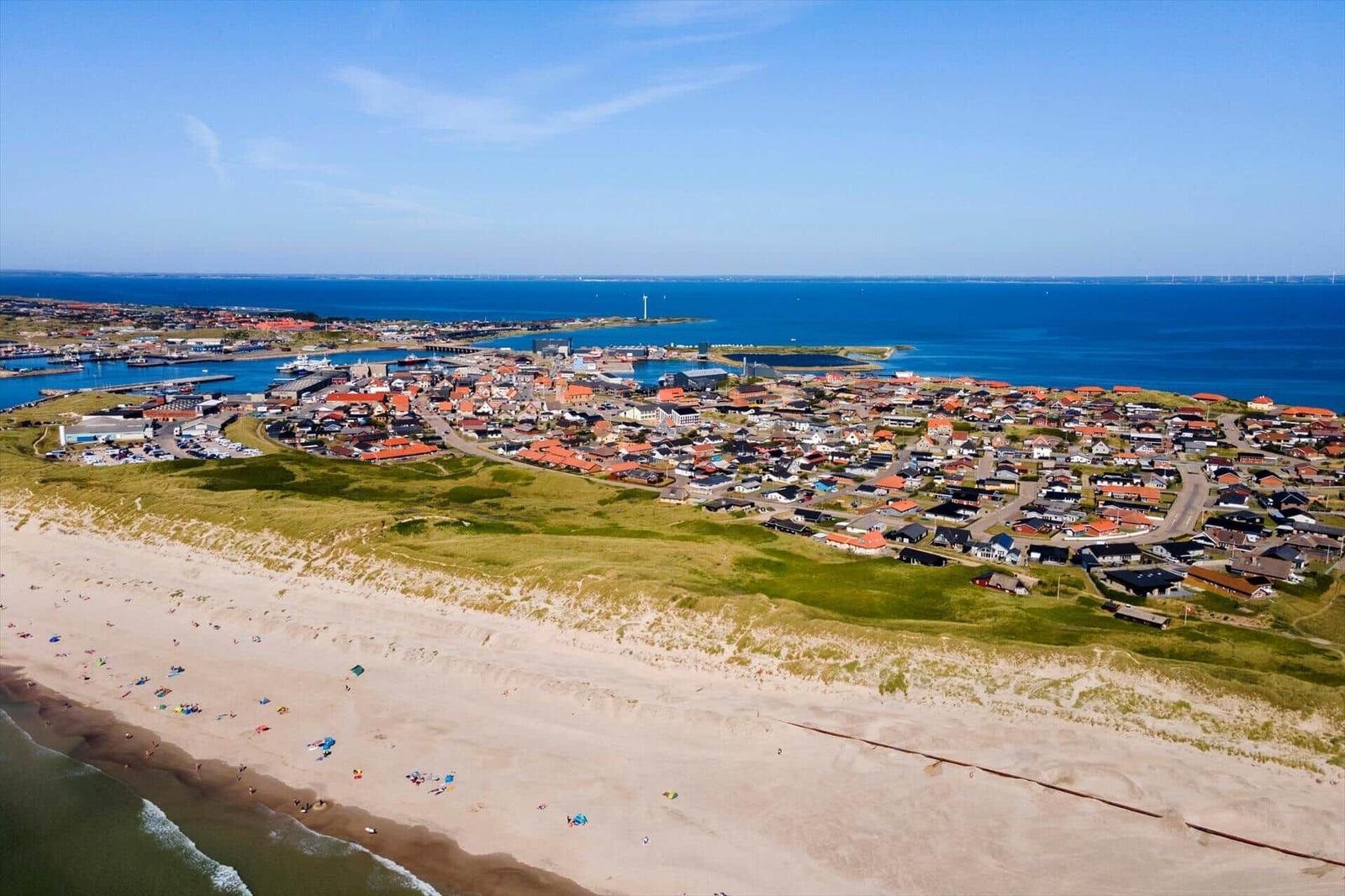 Strand mit Dünen und Küstenstadt mit Häusern und Hafen.