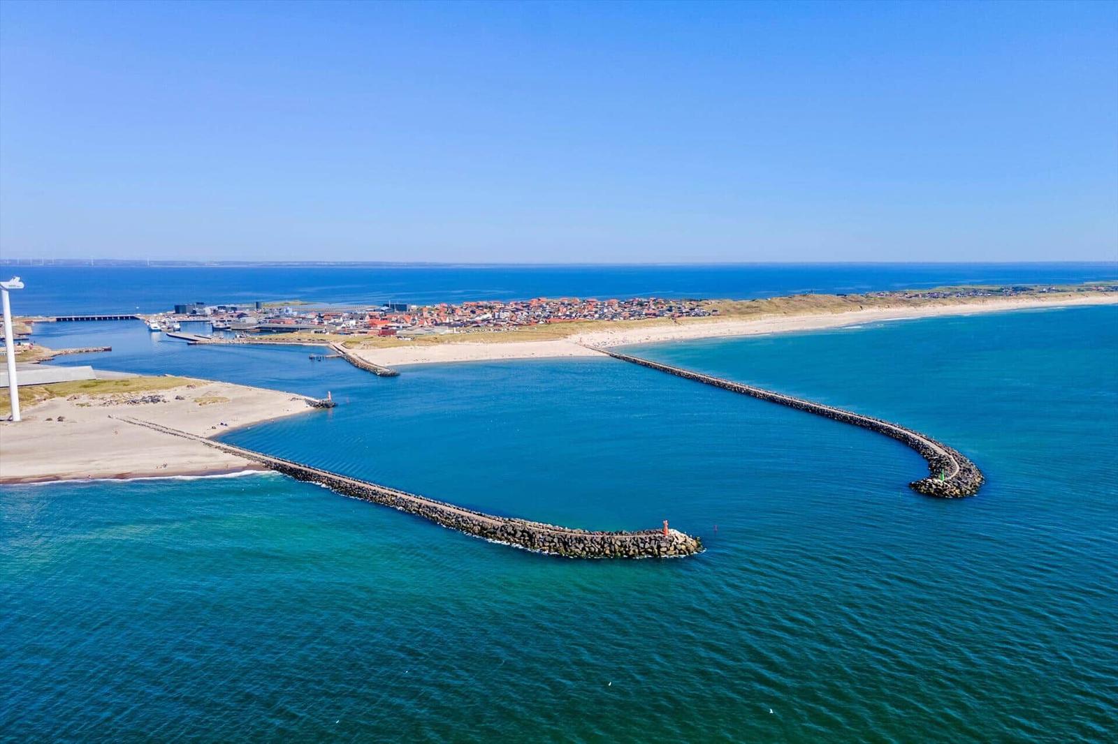 Ausblick auf Hafen und Strand mit Steinsperre und Windrad.