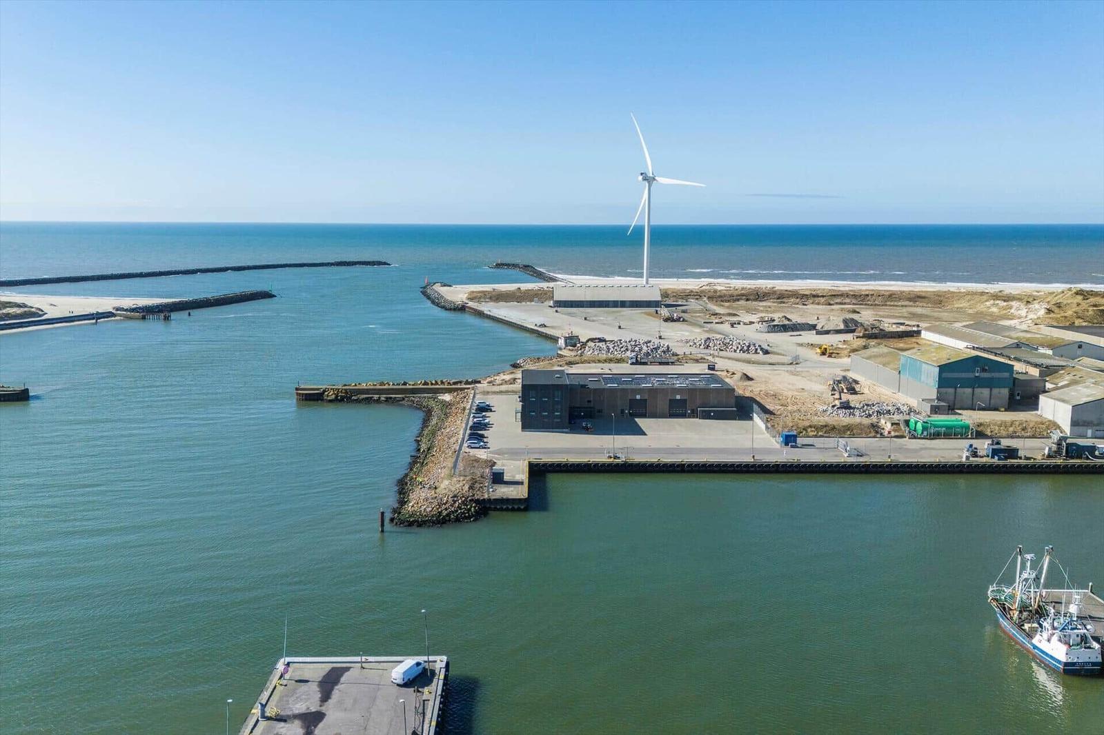 Hafen mit Windrad, Boot und Industriegebäuden an der Küste.